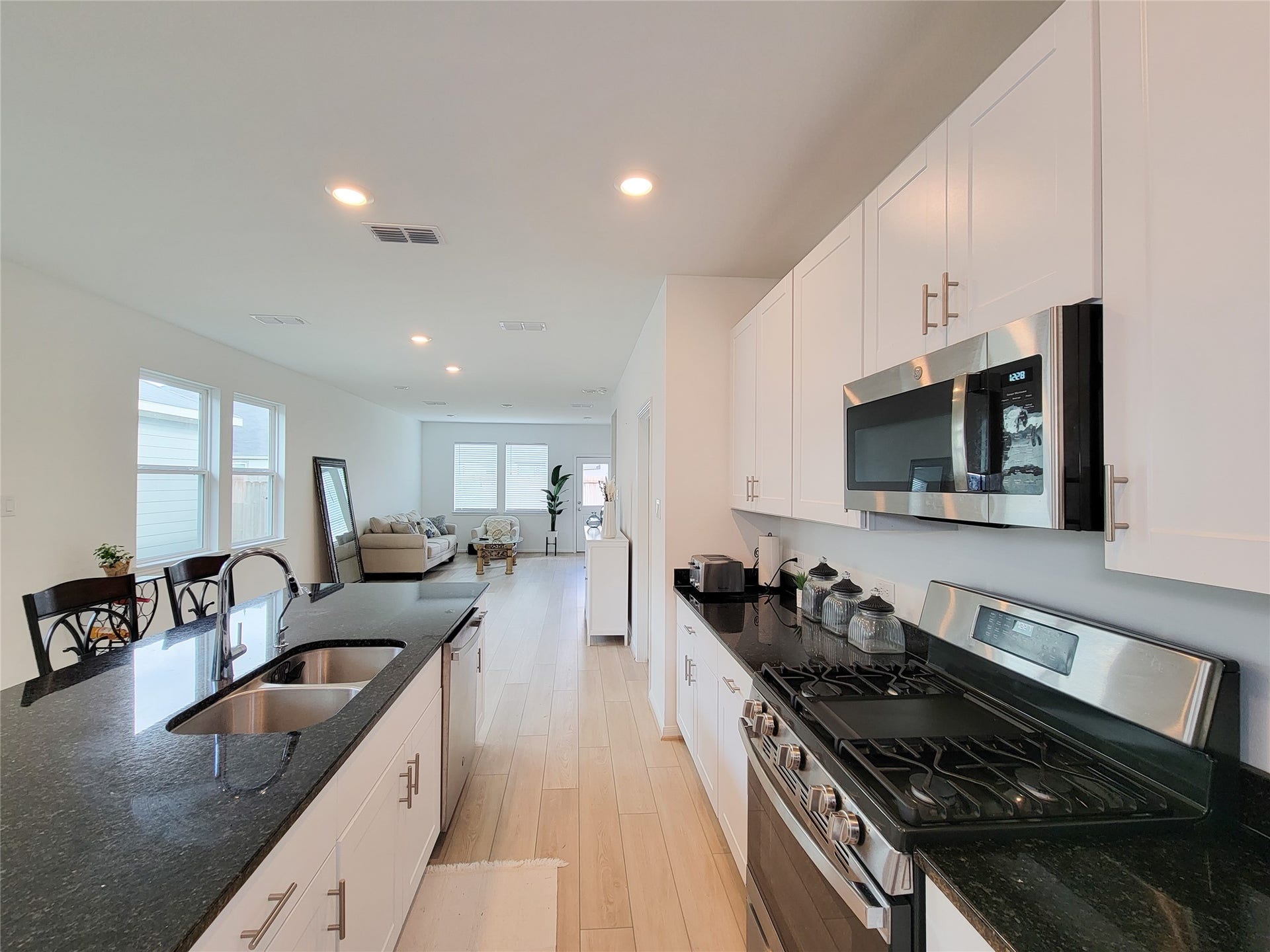 2719 Forest Retreat Lane, Missouri City, TX 77489 The kitchen features sleek black countertops, white cabinets, and stainless steel appliances. The space is bright with natural light from large windows, and there's a view of a cozy living room with contemporary furnishings.