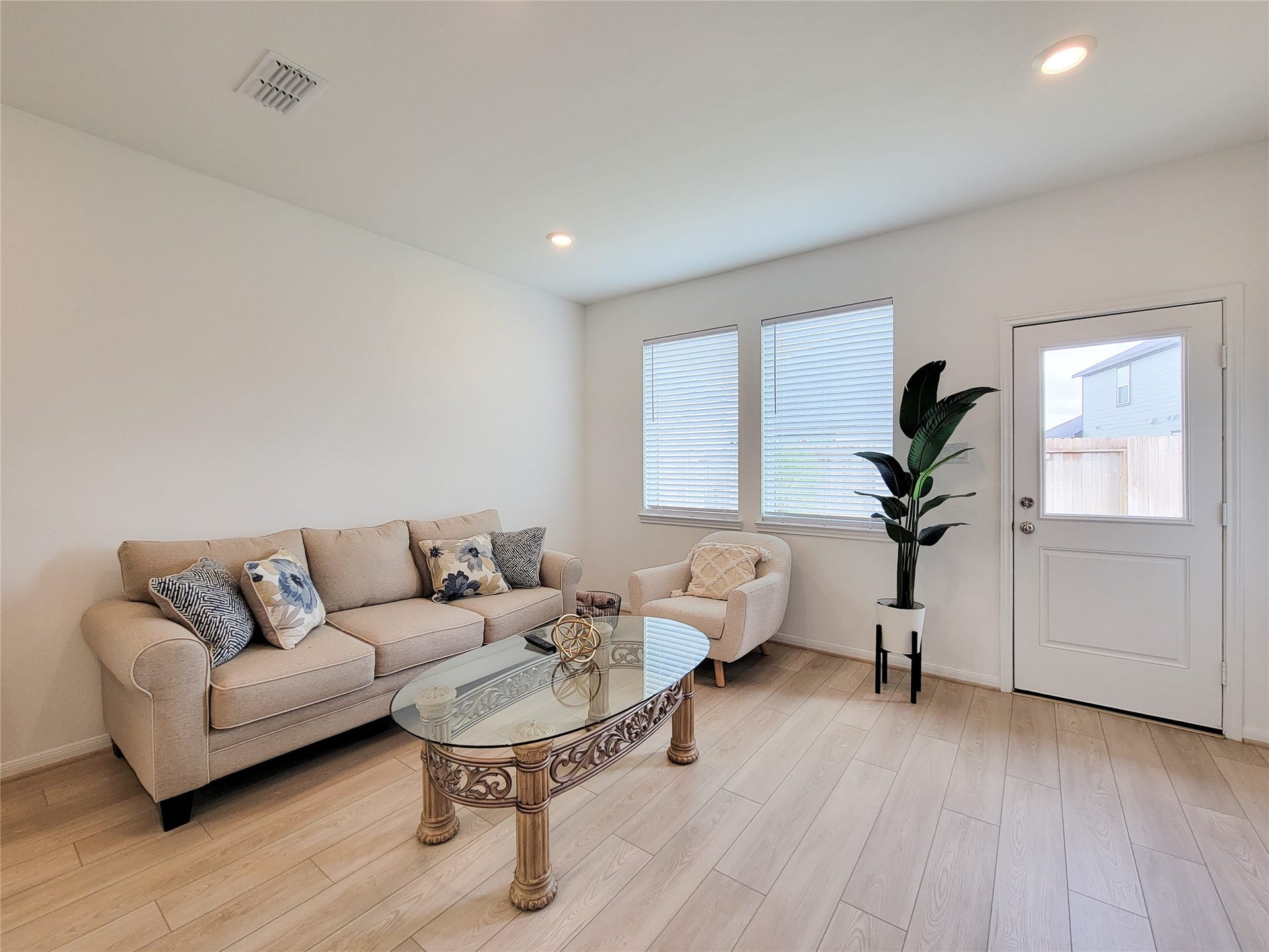 2719 Forest Retreat Lane, Missouri City, TX 77489 Bright and cozy living room with light wood flooring, featuring a comfortable beige sofa and armchair. The space is accented by large windows with blinds, recessed lighting.