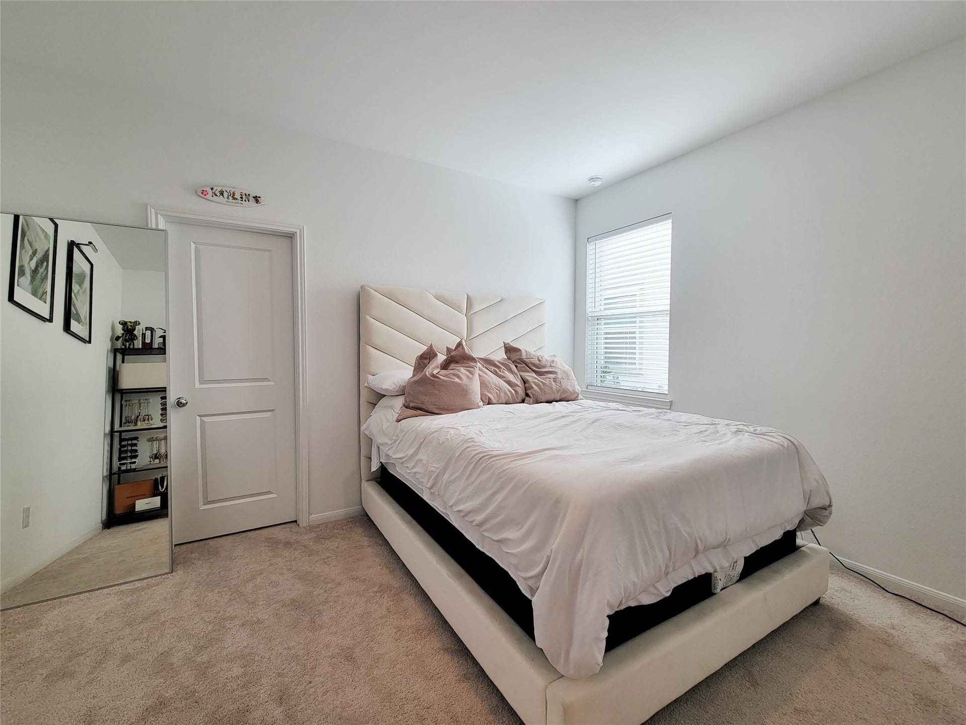 2719 Forest Retreat Lane, Missouri City, TX 77489 This bedroom features a cozy space with a plush carpet and a stylish, modern bed. It has a large window for natural light, a wall mirror, and a simple, clean design with white walls and minimalist decor.