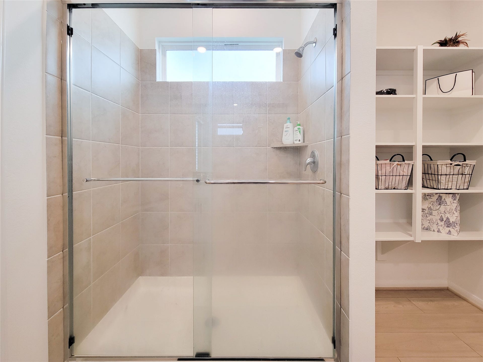 2719 Forest Retreat Lane, Missouri City, TX 77489 Modern bathroom with a spacious tiled shower featuring a glass door and built-in shelf. Adjacent open shelving provides convenient storage options.
