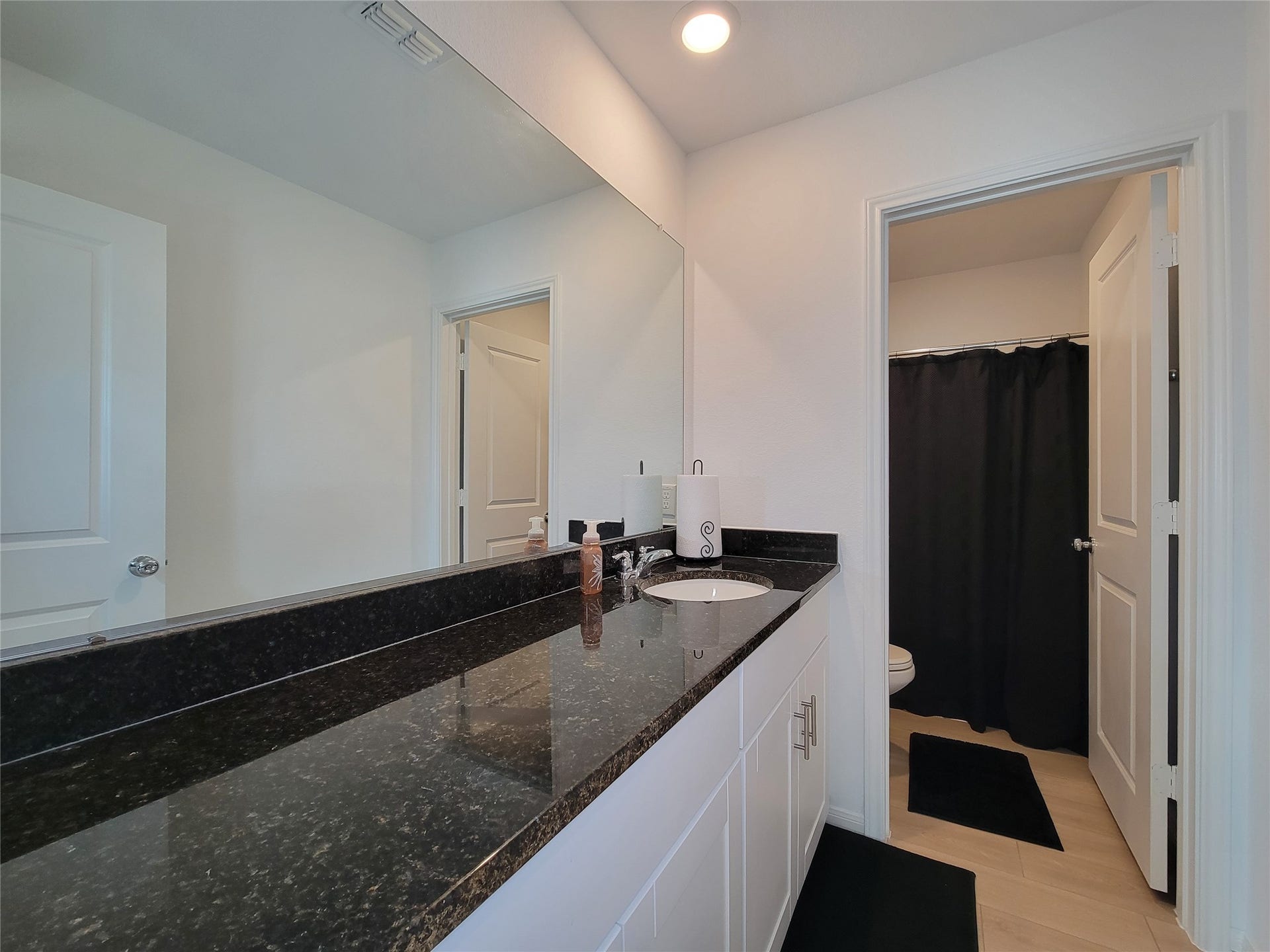 2719 Forest Retreat Lane, Missouri City, TX 77489 This bathroom features a sleek design with a wide black granite countertop, a large mirror, and white cabinetry. It includes a single sink and access to a shower.