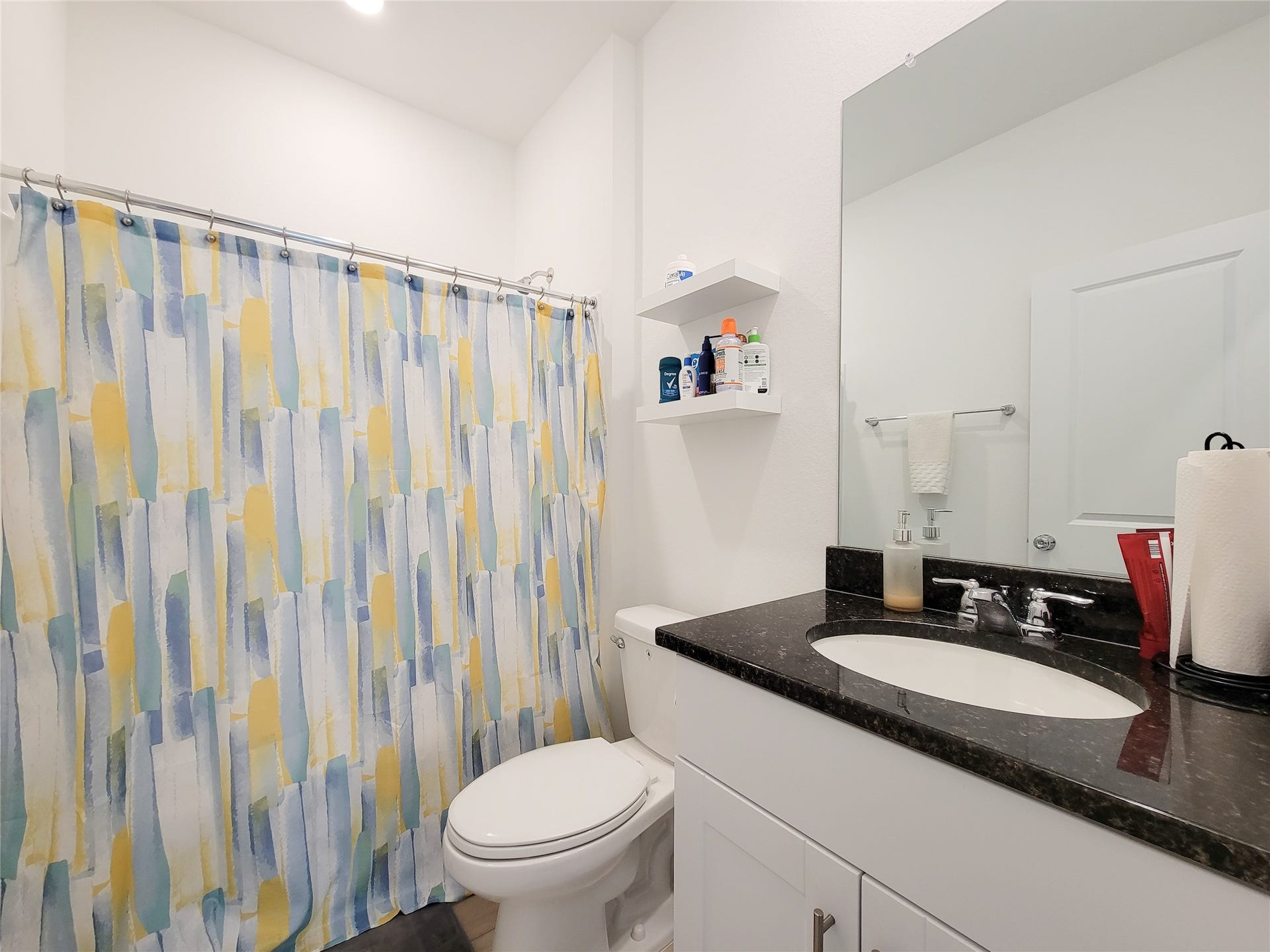 2719 Forest Retreat Lane, Missouri City, TX 77489 This secondary bathroom features a modern design with a sleek black countertop, white cabinetry, and a large mirror. It includes a shower and shelving for storage, providing both functionality and style.