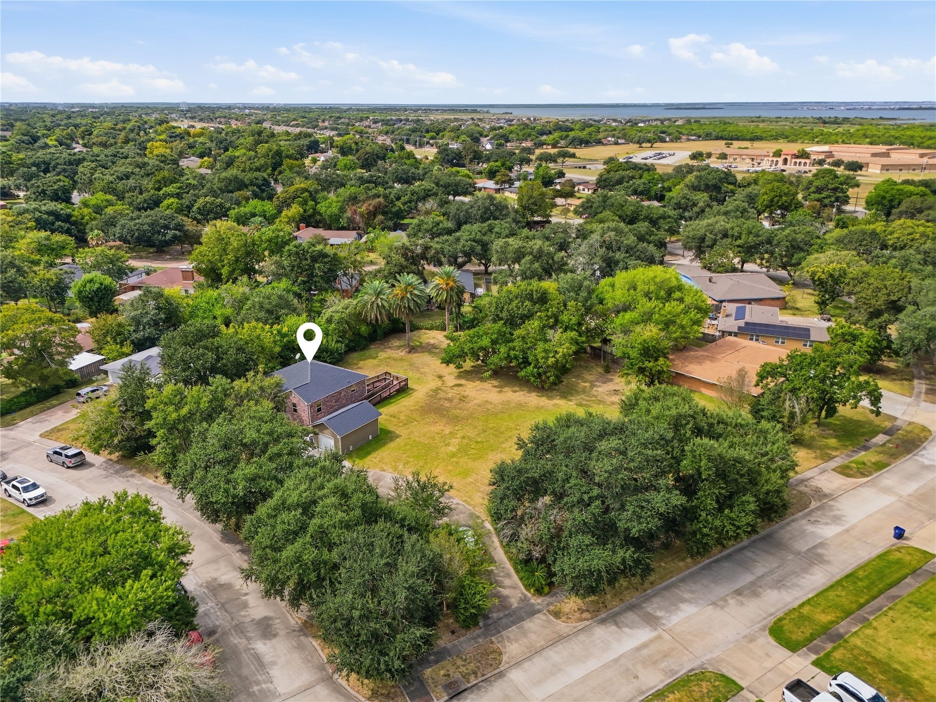102 20th Avenue N, Texas City, TX 77590 The large corner lot offers open yard space surrounded by mature trees and palms, with a curved driveway leading to the detached garage.