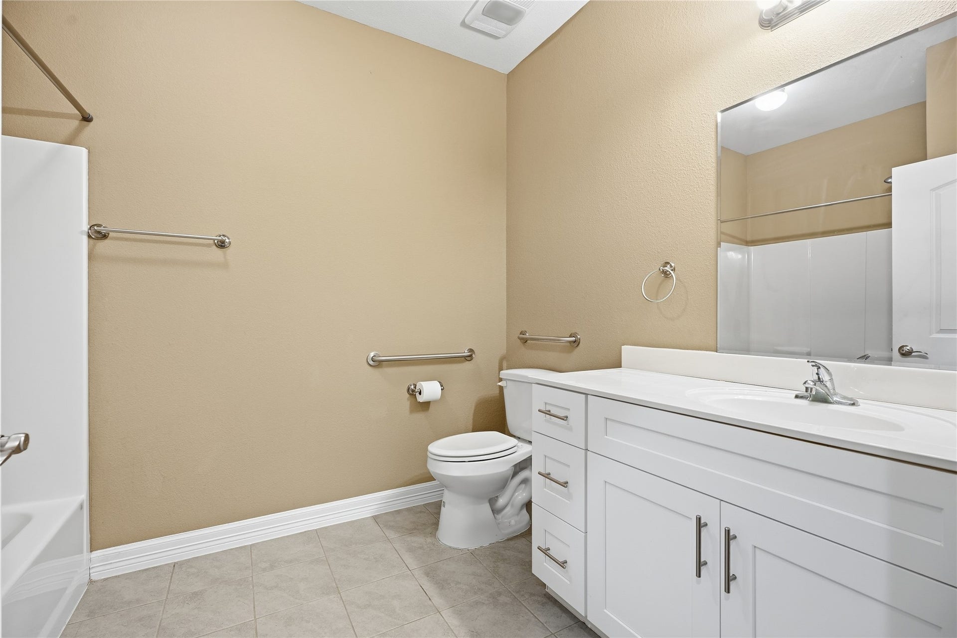 102 20th Avenue N, Texas City, TX 77590 Located between the two additional bedrooms and easily accessed from the main living area, this bathroom features a white vanity with drawer and cabinet storage, a large mirror, and grab bars beside the toilet.