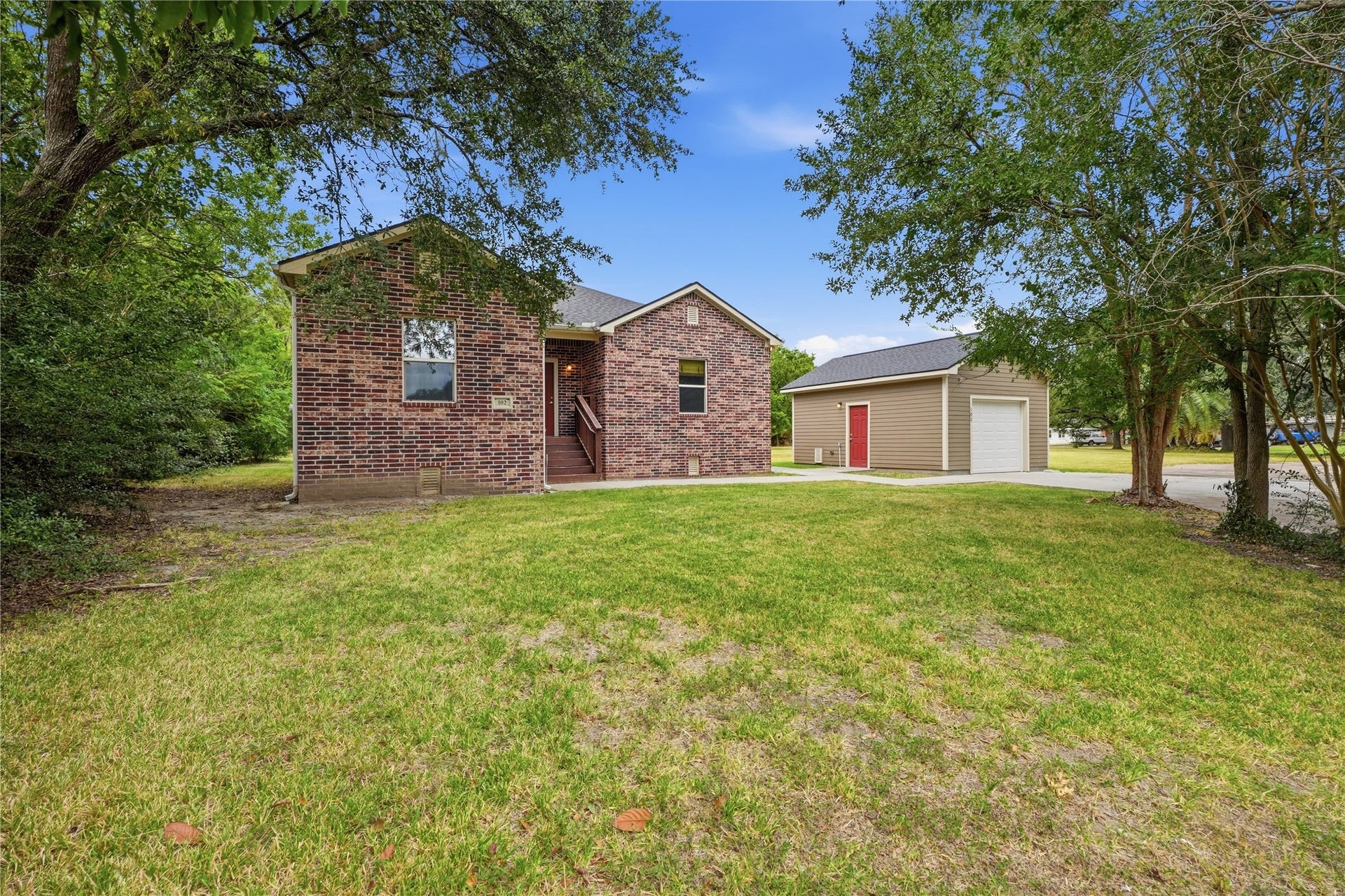 102 20th Avenue N, Texas City, TX 77590 Mature trees frame this brick home, with a spacious front yard, covered entry, and detached garage beside the driveway.