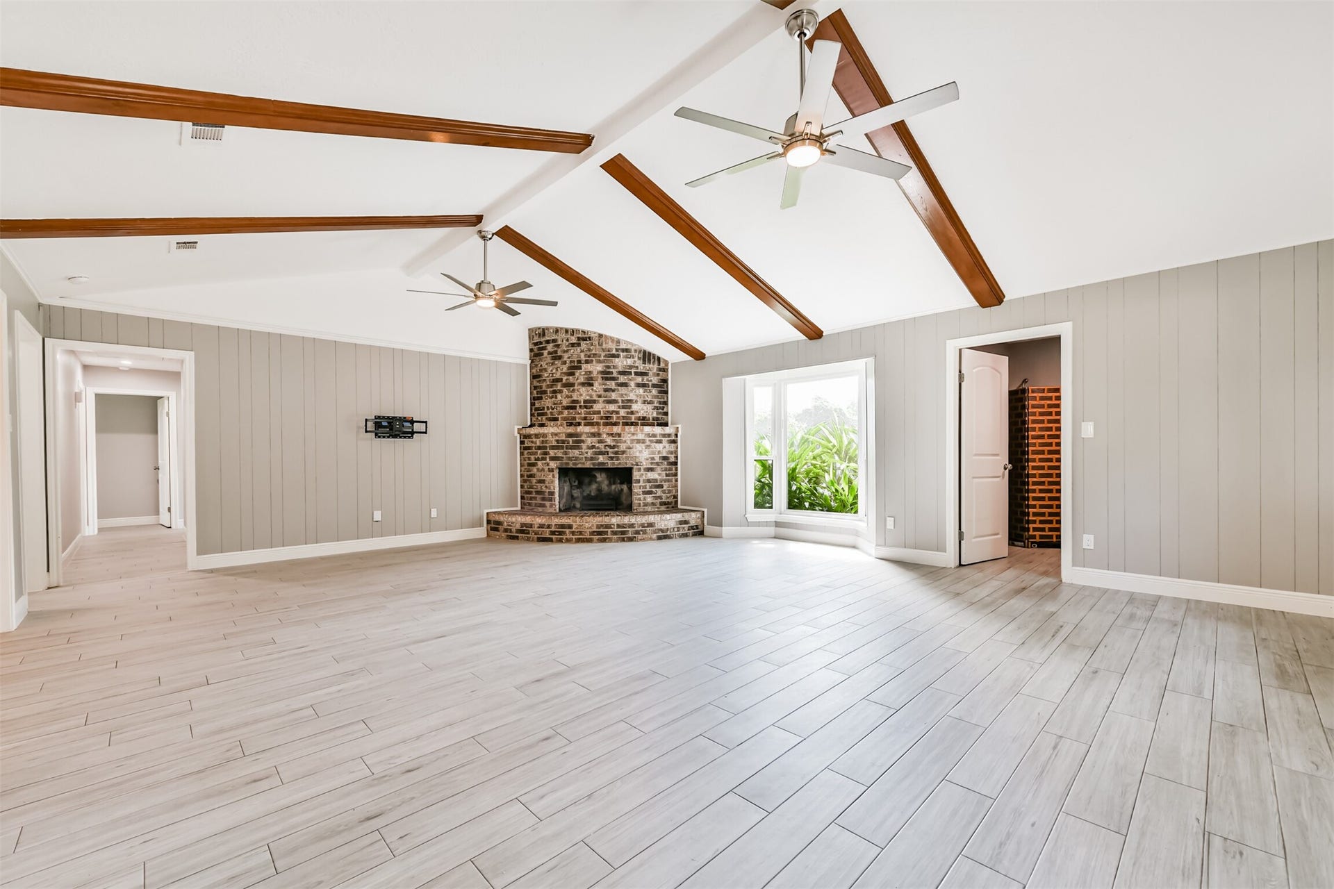 9311 Masters Road, Manvel, TX 77578 Spacious and inviting living area featuring high ceilings with elegant wood beams, a charming brick fireplace, and abundant natural light. Perfect for entertaining and relaxing.
