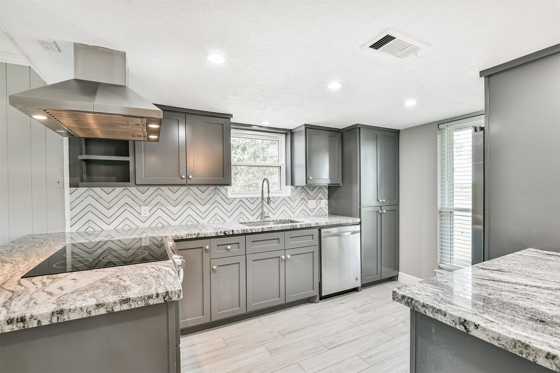 9311 Masters Road, Manvel, TX 77578 Modern kitchen featuring sleek gray cabinets, elegant herringbone backsplash, and stunning granite countertops. Abundant natural light and top-of-the-line appliances create a perfect space for culinary creativity.