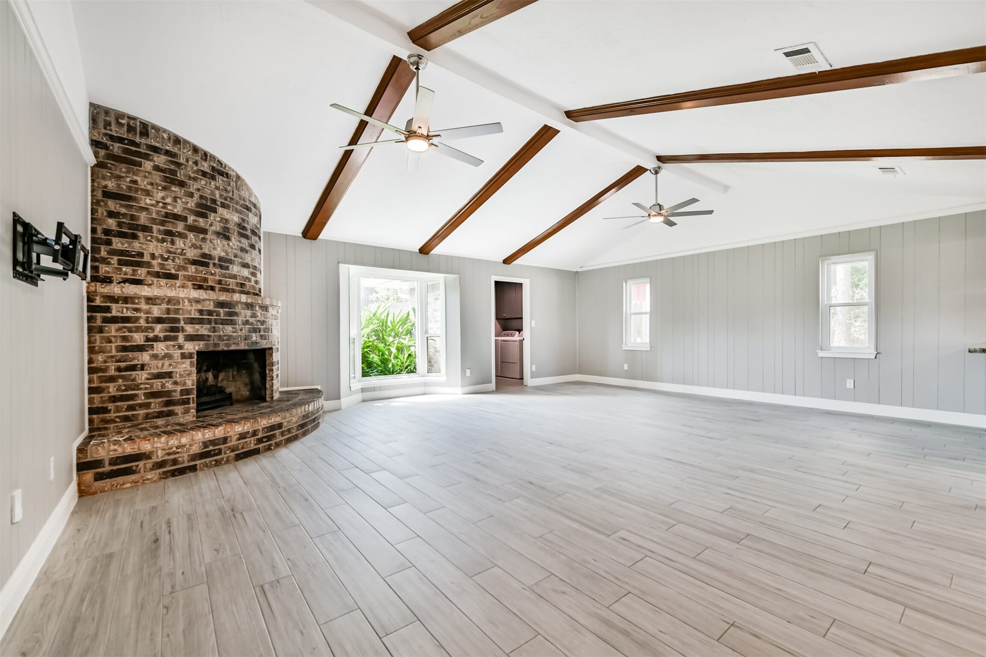 9311 Masters Road, Manvel, TX 77578 Spacious living area featuring vaulted ceilings with elegant wood beams, a stunning brick fireplace, and abundant natural light from large windows. Perfect for relaxing or entertaining.