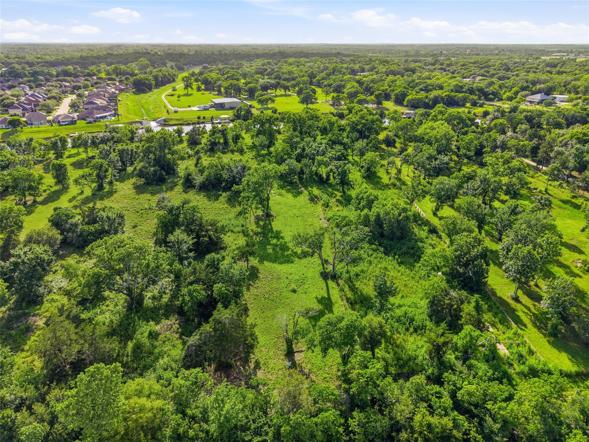 7326 Custer Street, Hitchcock, TX 77563 This aerial photo showcases a lush, expansive green area with scattered trees, offering a serene, natural setting.