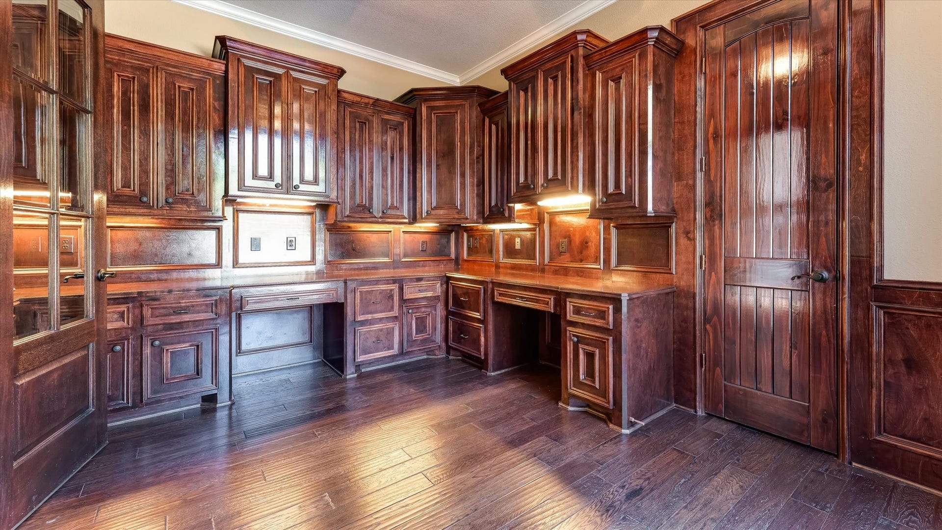 8071 Stacy Diane Drive, Montgomery, TX 77316 This photo showcases a luxurious home office with rich wood cabinetry, built-in desks, and elegant wood paneling. The space is well-lit with under-cabinet lighting, offering a warm and sophisticated atmosphere perfect for productivity.