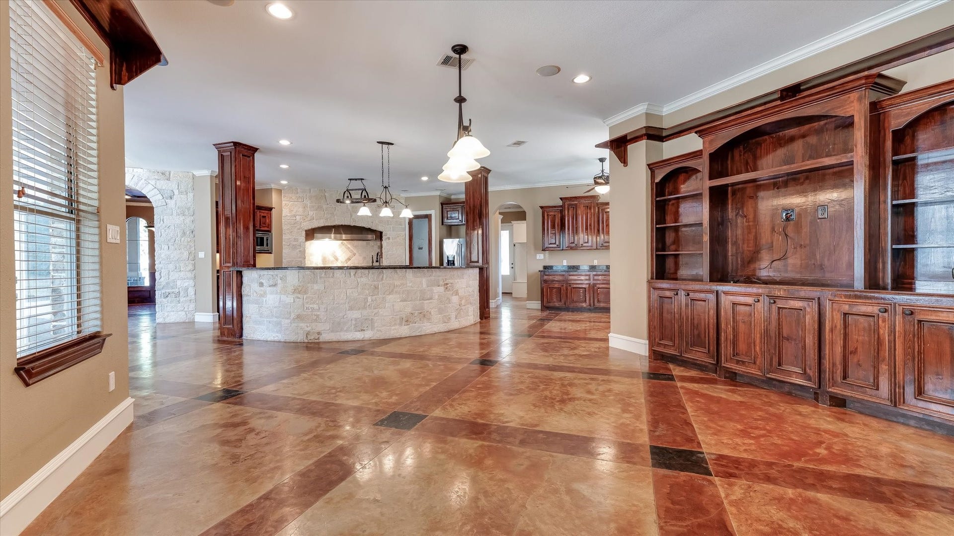 8071 Stacy Diane Drive, Montgomery, TX 77316 This spacious open-concept living area features elegant stone accents, rich wood cabinetry, and a large built-in entertainment center. The kitchen boasts a curved island with pendant lighting, providing a warm and inviting atmosphere ideal for entertaining.