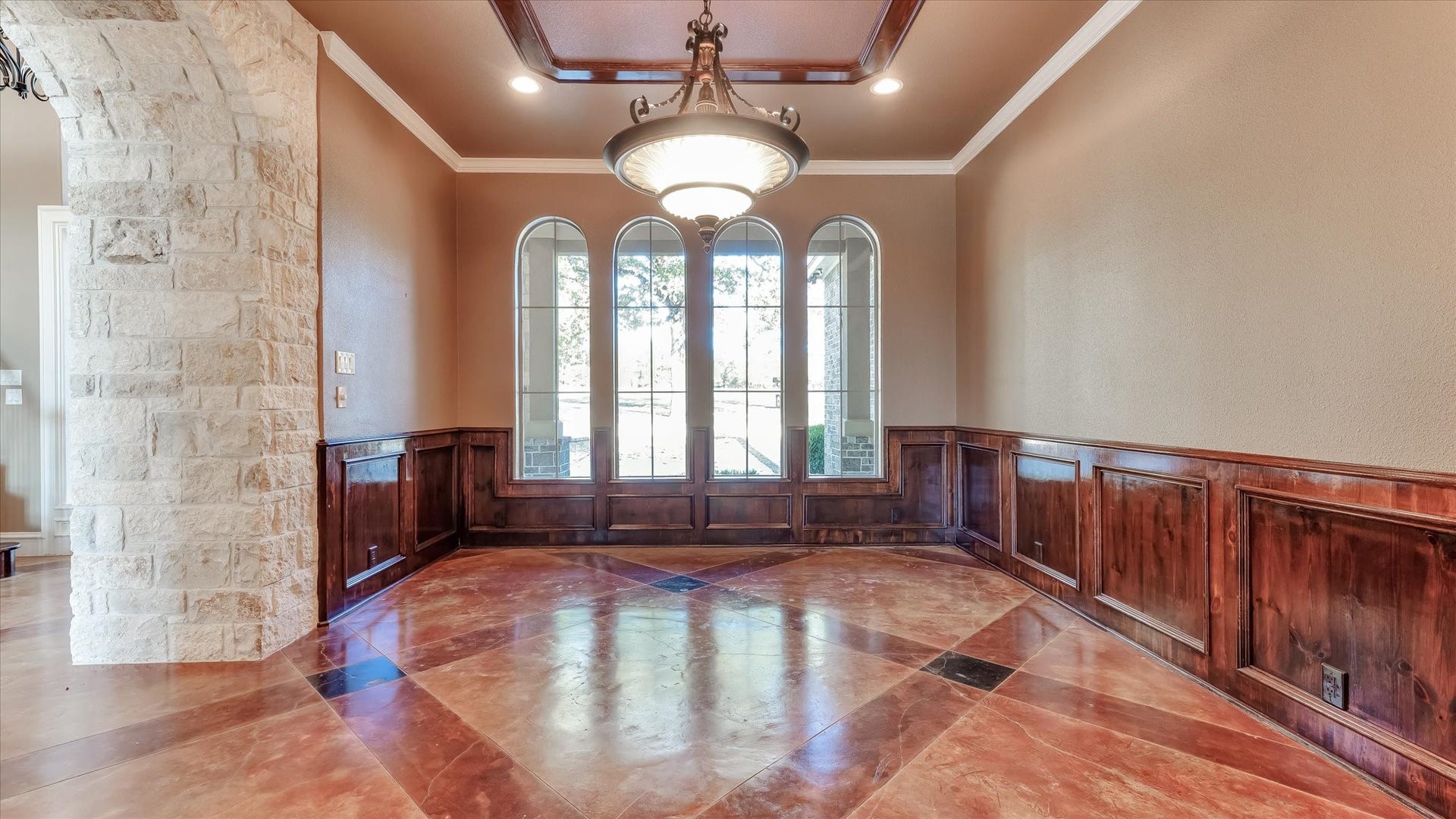 8071 Stacy Diane Drive, Montgomery, TX 77316 This elegant room features rich wood paneling and a stone archway, complemented by large arched windows that allow natural light to flood in. The ornate ceiling fixture and polished tile flooring add a touch of luxury, creating a welcoming and sophisticated atmosphere.