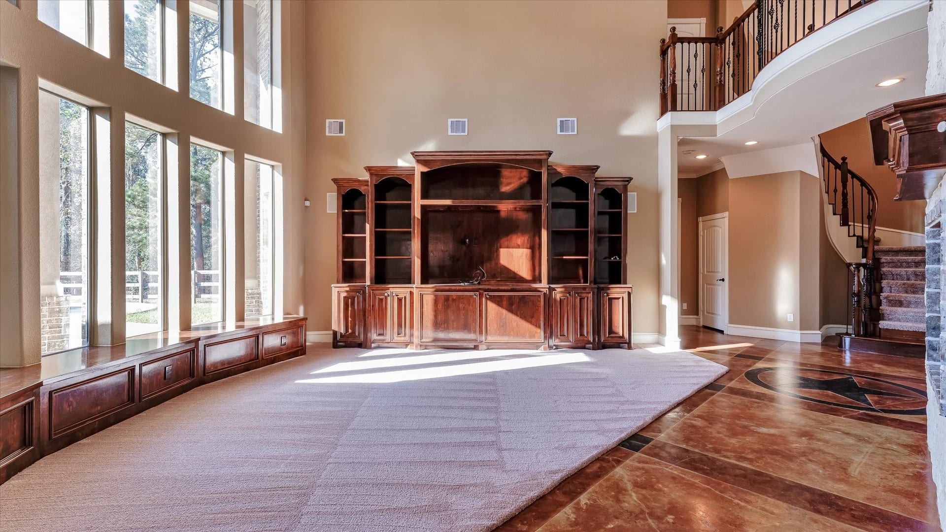 8071 Stacy Diane Drive, Montgomery, TX 77316 This spacious living area features high ceilings, large windows with abundant natural light, and a grand wooden entertainment center. A curved staircase and elegant railing lead to the upper floor, while the polished floors and stylish design offer a luxurious feel.