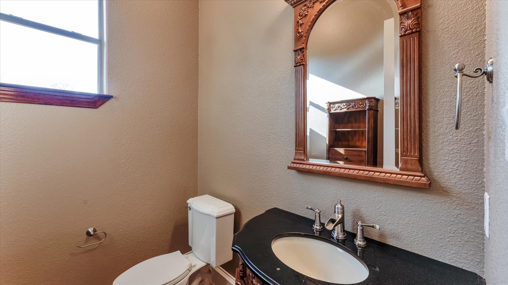 8071 Stacy Diane Drive, Montgomery, TX 77316 This bathroom features a classic design with a stylish wooden-framed mirror, a granite countertop with a sink, and a modern toilet. It has a window for natural light and a towel holder for convenience.