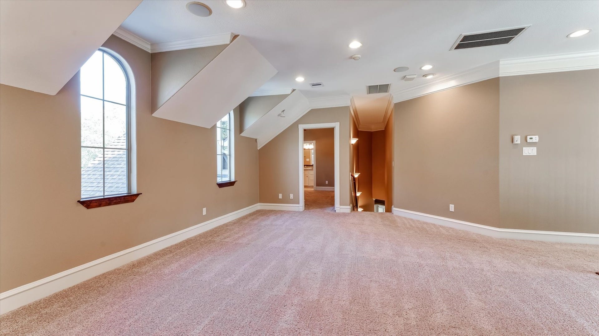 8071 Stacy Diane Drive, Montgomery, TX 77316 This spacious room features plush carpeting, neutral walls, and ample natural light from arched windows. Recessed lighting and crown molding add elegance, with a view into a connected area, suitable for a cozy living or entertainment space.