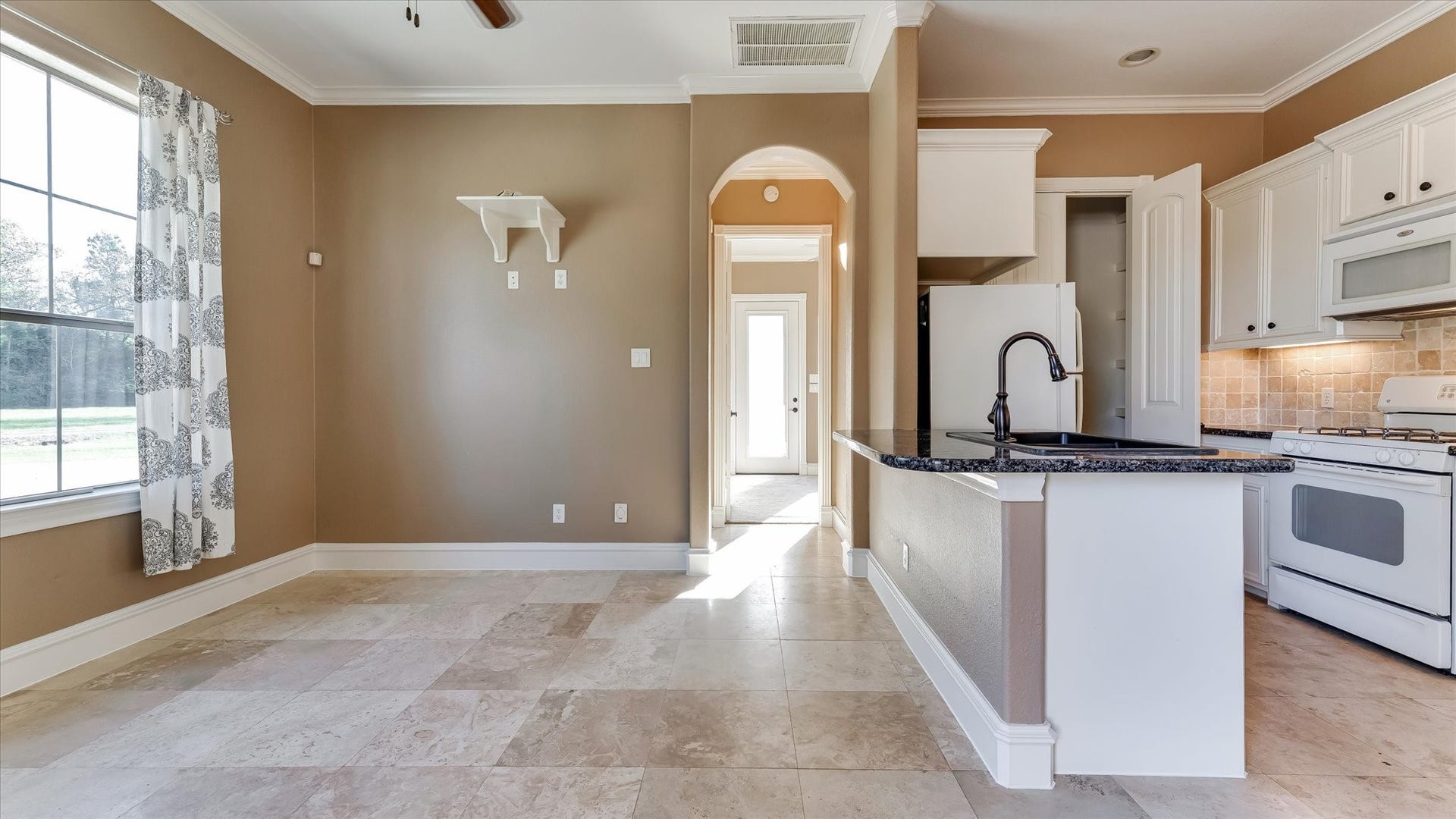 8071 Stacy Diane Drive, Montgomery, TX 77316 This photo showcases a bright, open kitchen with modern appliances, granite countertops, and tile flooring. It features a large window for natural light, neutral wall colors, and a convenient layout with an archway leading to an adjacent room.