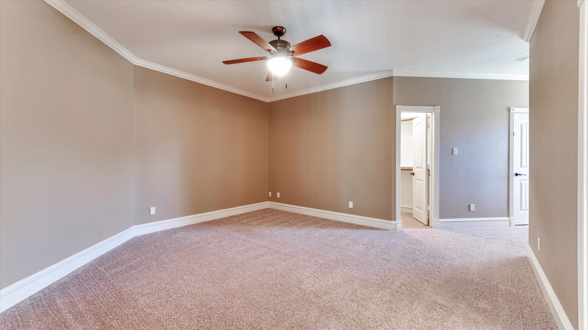 8071 Stacy Diane Drive, Montgomery, TX 77316 Spacious bedroom with neutral walls and carpet, featuring a ceiling fan and crown molding. The room has ample natural light and access to a connecting hallway or room through a white door.