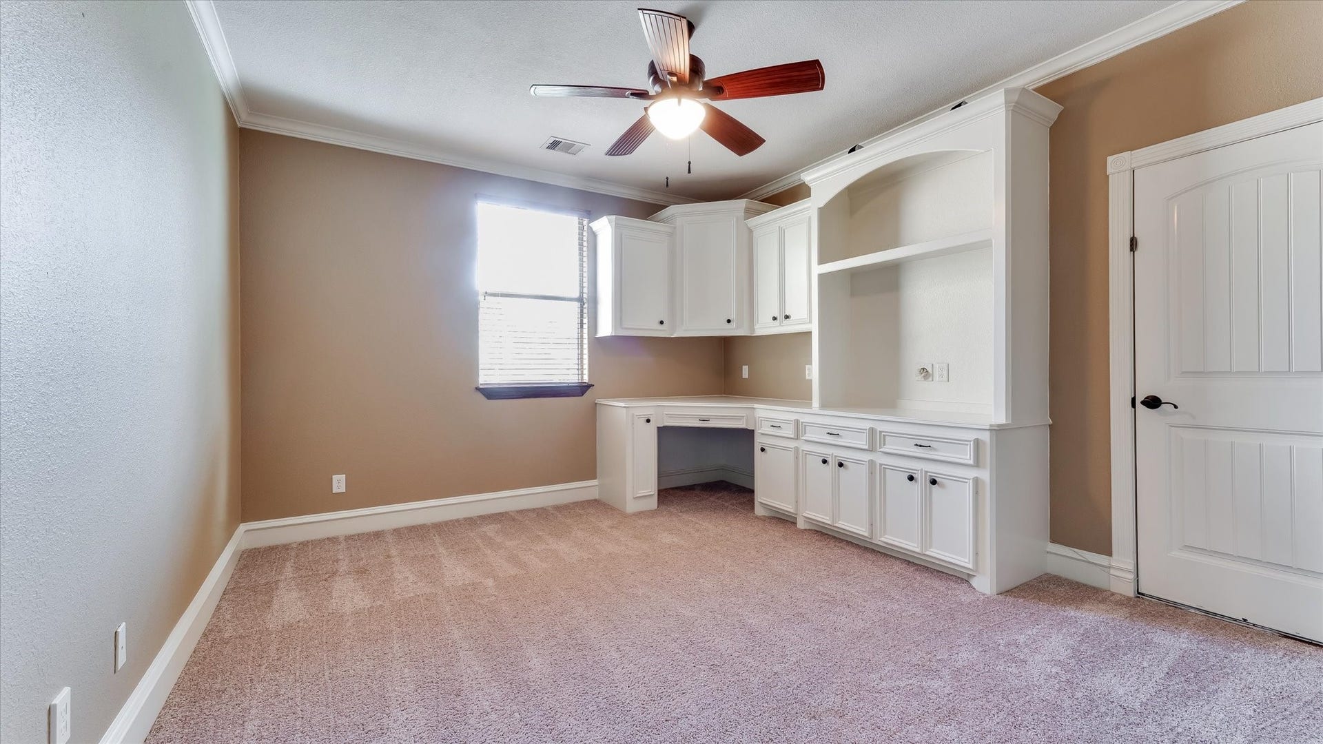 8071 Stacy Diane Drive, Montgomery, TX 77316 This room features neutral-toned walls and carpet, with built-in white cabinetry and a desk for ample storage and workspace. A ceiling fan adds comfort, and a window provides natural light. Perfect for a home office or study.