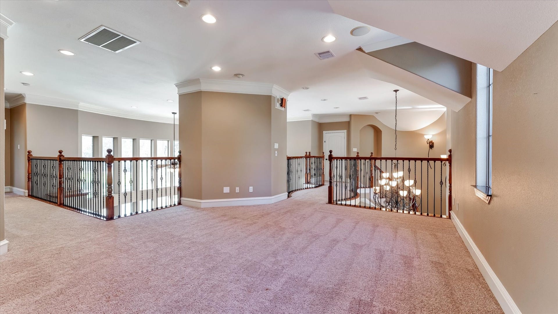 8071 Stacy Diane Drive, Montgomery, TX 77316 This photo showcases a spacious upstairs landing with plush carpeting and elegant iron railings overlooking a lower level. Ample natural light streams through multiple windows, and recessed lighting adds a modern touch. The area is open and versatile, suitable for a sitting area or home office.