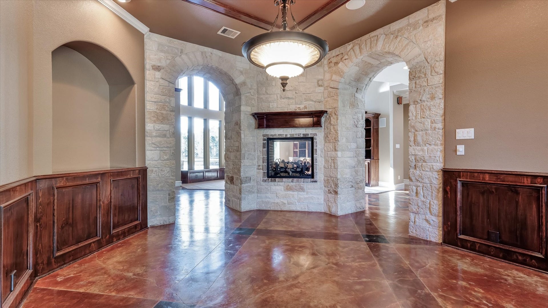 8071 Stacy Diane Drive, Montgomery, TX 77316 This elegant room features a stone fireplace and arched doorways, complemented by rich wood paneling and a striking chandelier. Large windows offer ample natural light, enhancing the warm, inviting atmosphere.