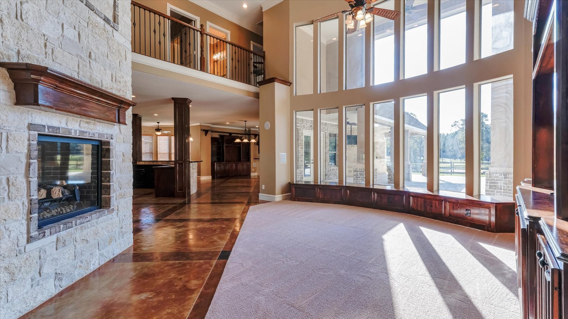 8071 Stacy Diane Drive, Montgomery, TX 77316 This spacious living area features a stunning wall of floor-to-ceiling windows, allowing ample natural light and showcasing outdoor views. It includes a stone fireplace, high ceilings, and an open layout leading to a balcony and adjoining rooms, perfect for entertaining and relaxation.