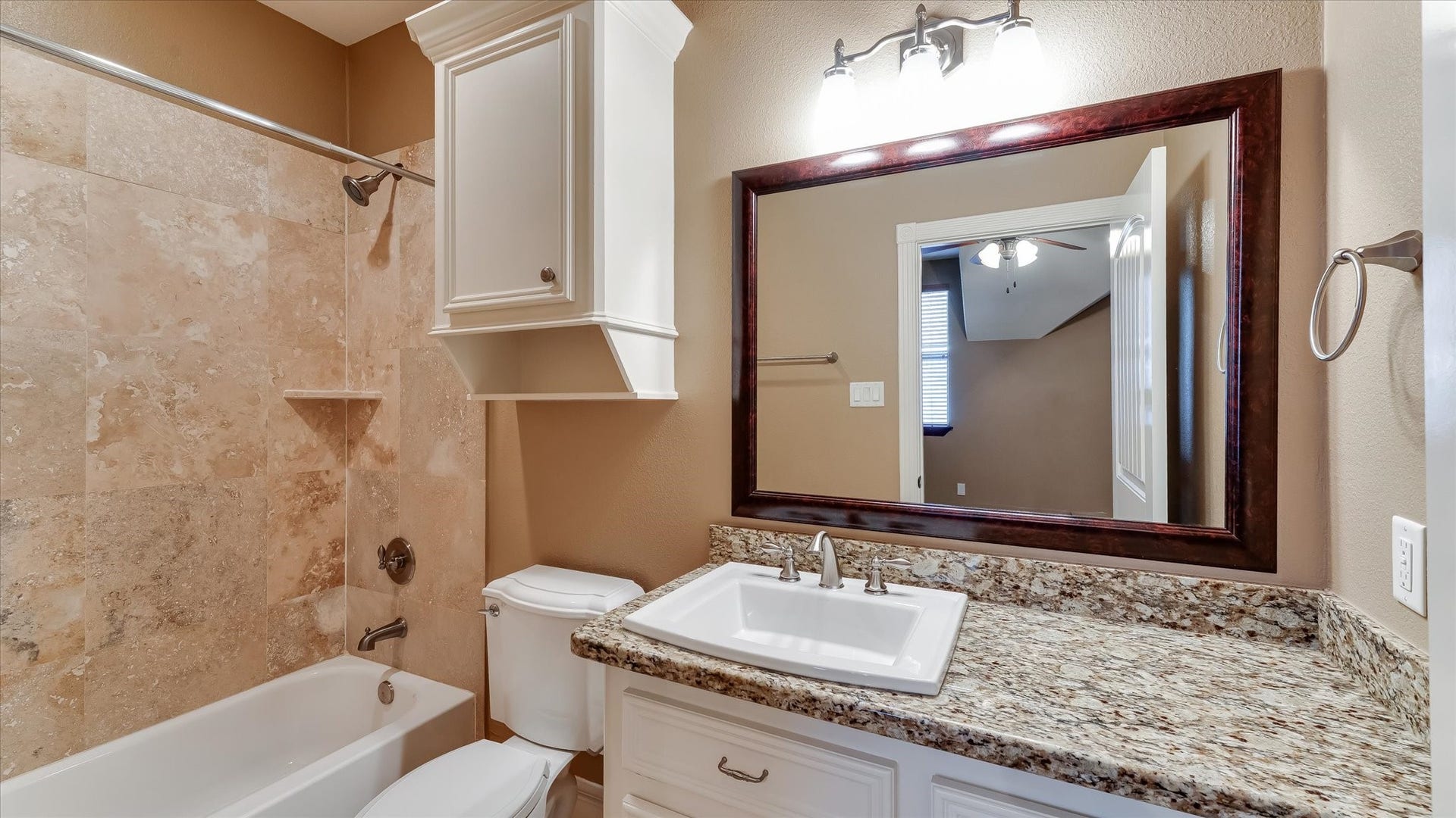8071 Stacy Diane Drive, Montgomery, TX 77316 This bathroom features a granite countertop with an undermount sink, a large framed mirror, and a bathtub with beige tile surround. The space is well-lit with modern fixtures and includes a storage cabinet above the toilet.