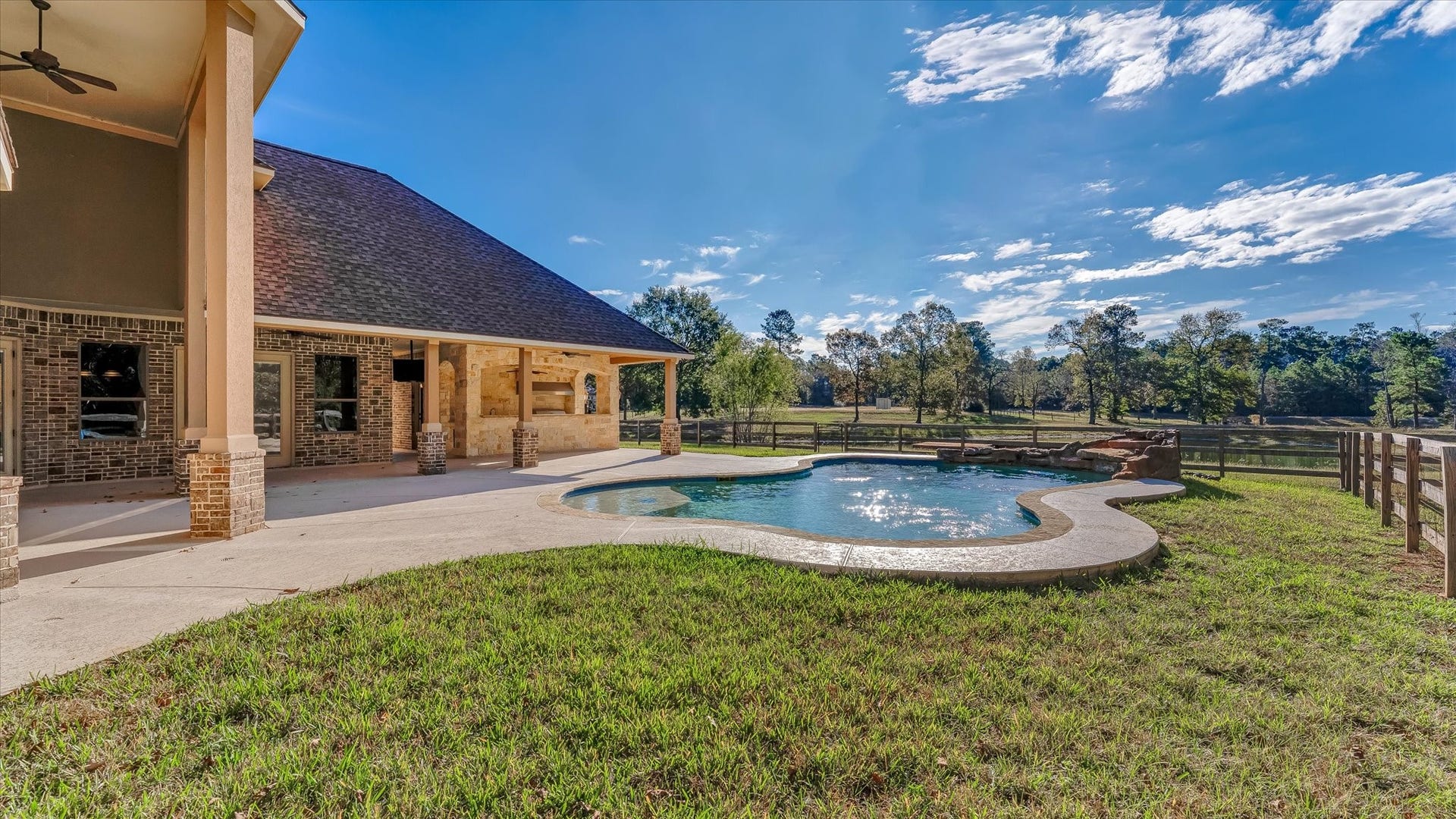8071 Stacy Diane Drive, Montgomery, TX 77316 This photo showcases a beautiful backyard with a spacious covered patio and a uniquely shaped pool. It's surrounded by lush greenery and has a scenic view of open fields and trees, offering a serene and private outdoor space.