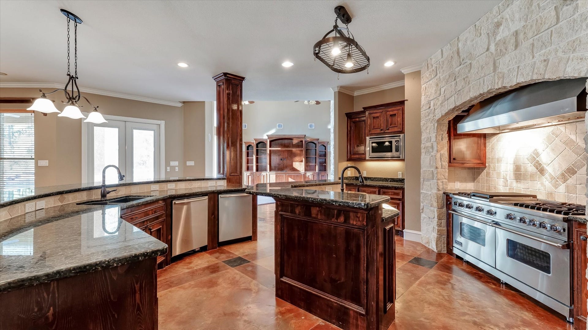 8071 Stacy Diane Drive, Montgomery, TX 77316 This spacious kitchen features elegant dark wood cabinetry, a large center island, and granite countertops. It includes a professional-grade stainless steel range, a unique stone accent wall, and abundant natural light from large windows and glass doors.