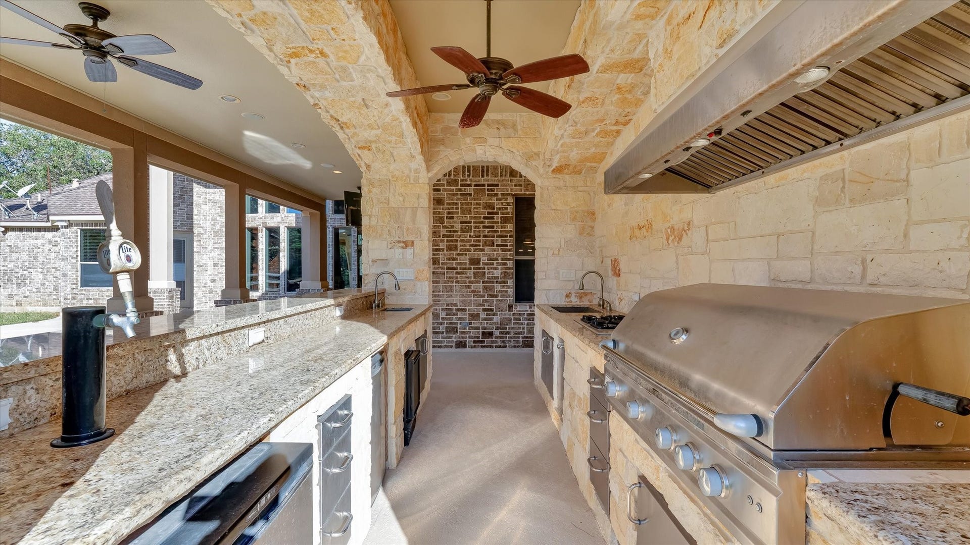 8071 Stacy Diane Drive, Montgomery, TX 77316 This photo showcases a luxurious outdoor kitchen with a stone and brick design, featuring granite countertops, stainless steel appliances, a built-in grill, and ceiling fans, all under a covered patio perfect for entertaining.