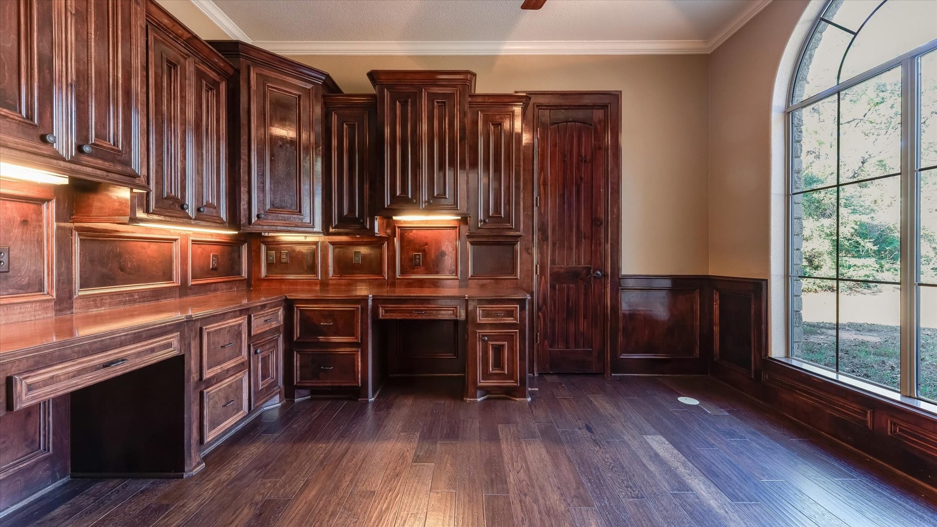 8071 Stacy Diane Drive, Montgomery, TX 77316 This room features rich wood cabinetry and flooring, offering ample storage and workspace. A large arched window provides natural light, enhancing its warm, elegant atmosphereideal for a home office or study.