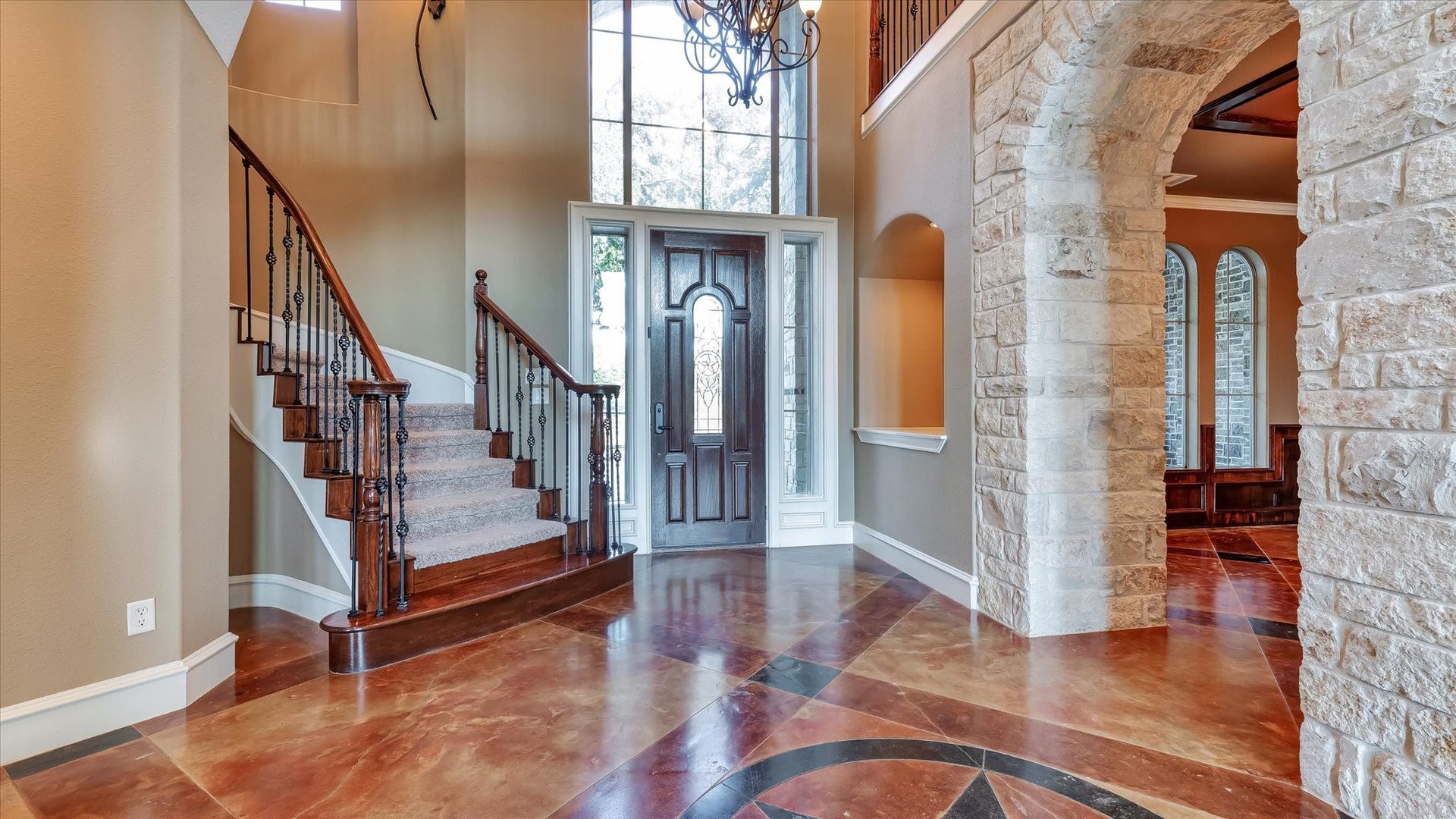 8071 Stacy Diane Drive, Montgomery, TX 77316 This photo showcases an elegant entryway with a curved staircase and wrought iron handrails. The space features a grand wooden door, high ceilings, and a stone archway leading to another room. The floor has a polished, patterned design, enhancing the luxurious feel.