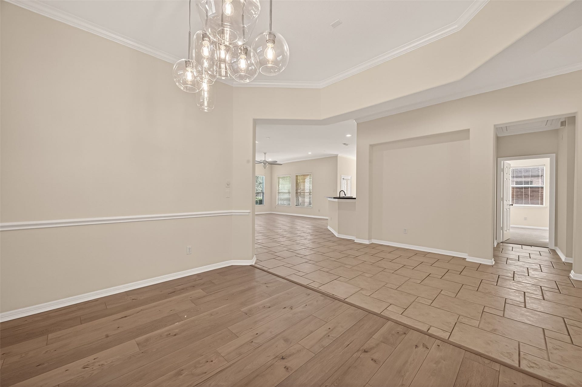 10106 Lost Hollow Lane, Missouri City, TX 77459 This photo showcases a spacious, open-plan living area with a blend of wood and tile flooring. It features modern lighting, neutral wall colors, and a ceiling fan, providing a versatile and inviting space. Large windows allow for ample natural light, enhancing the room's airy feel.