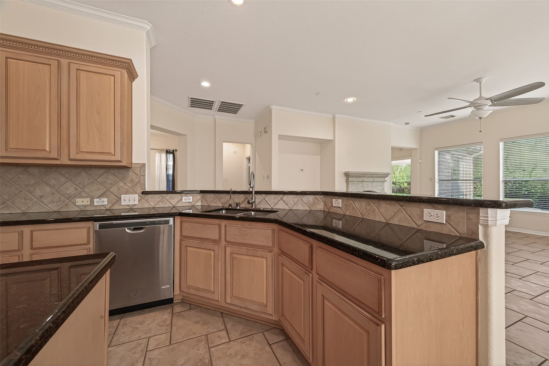 10106 Lost Hollow Lane, Missouri City, TX 77459 This spacious kitchen features granite countertops, light wood cabinetry, and stainless steel appliances. It opens to a bright living area with large windows and a ceiling fan, creating an inviting and functional space for entertaining.