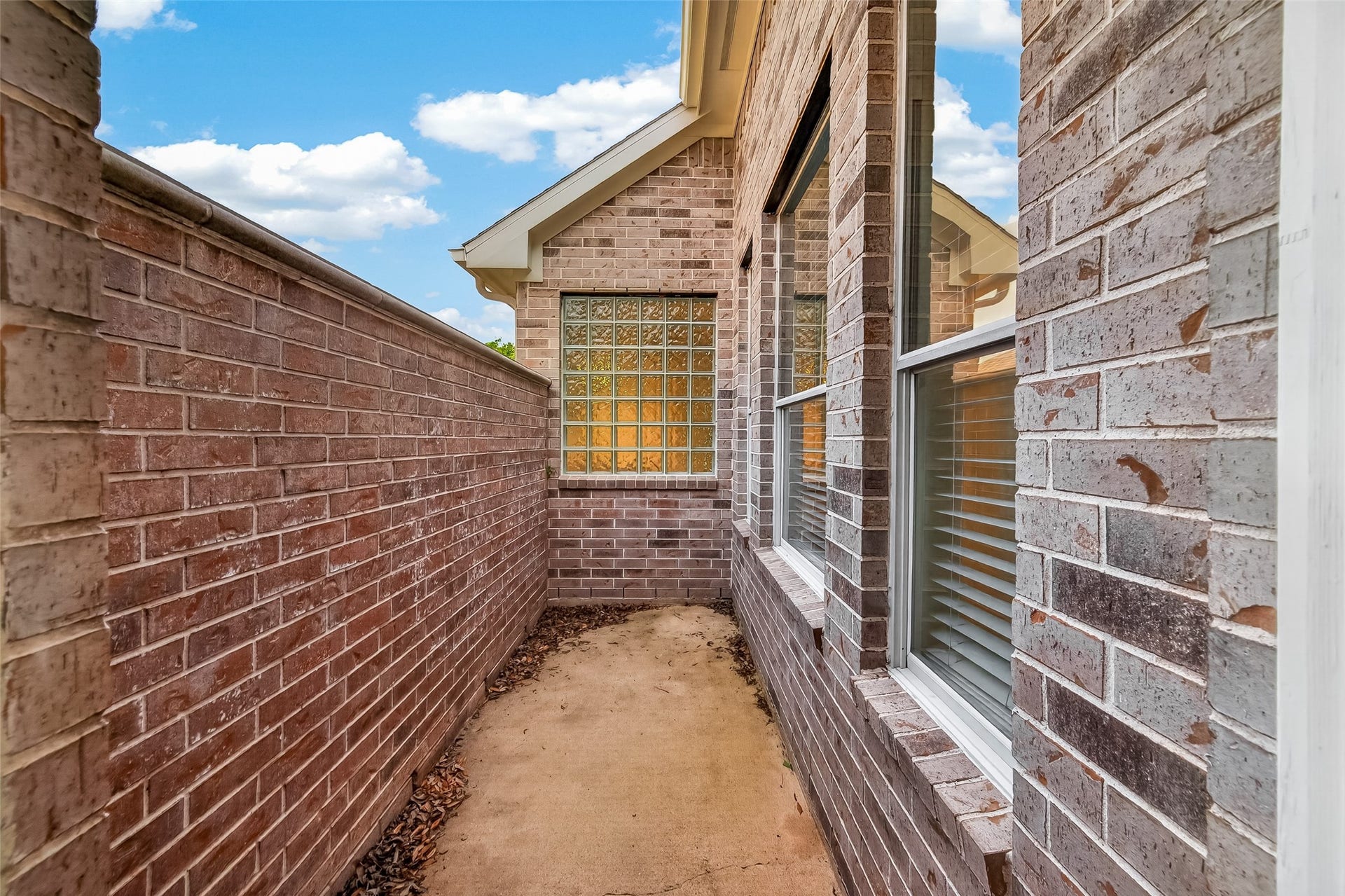 10106 Lost Hollow Lane, Missouri City, TX 77459 This photo shows a narrow brick-walled patio area with windows on one side, offering a private outdoor space.