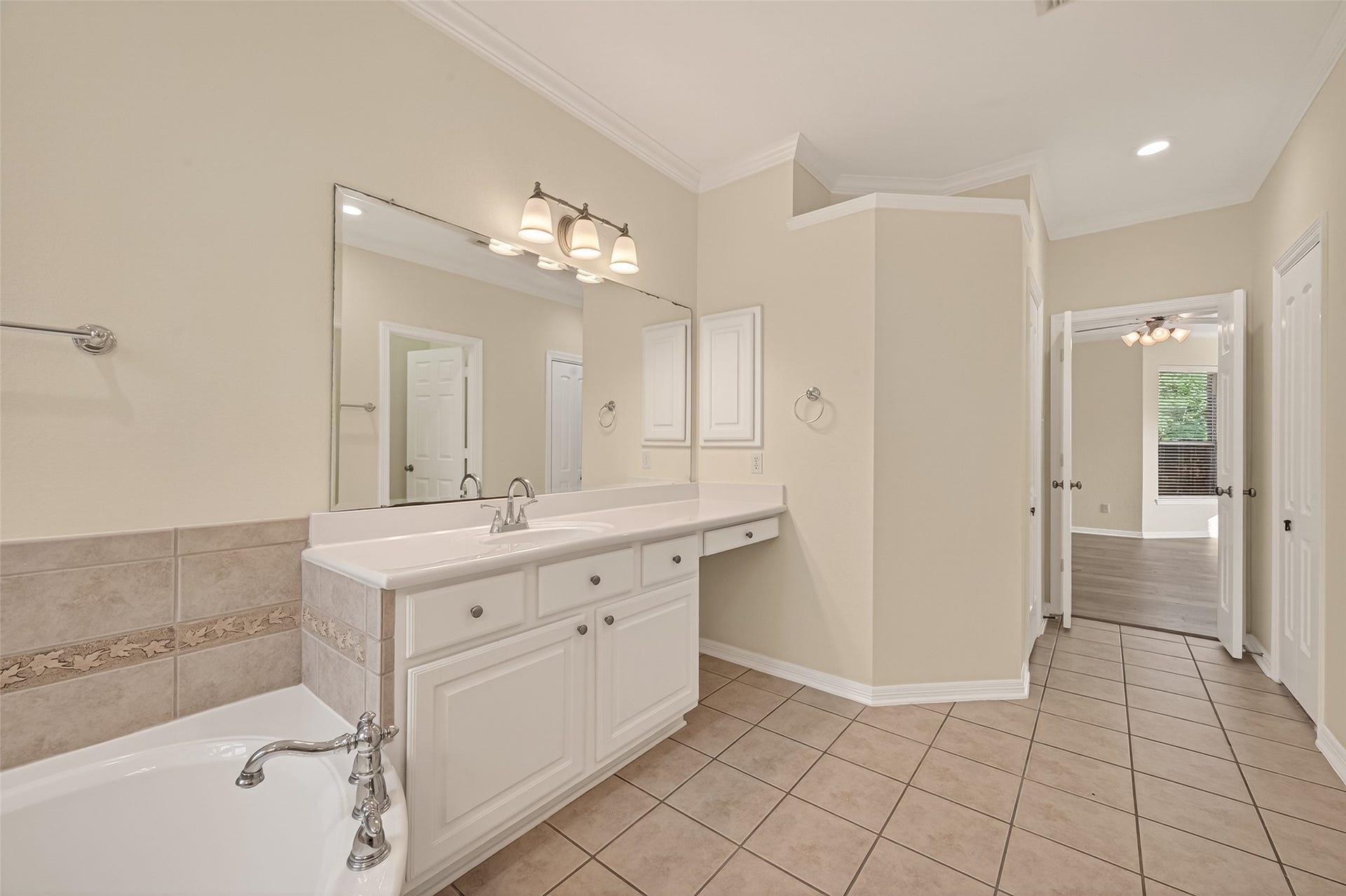 10106 Lost Hollow Lane, Missouri City, TX 77459 This photo showcases a spacious primary bathroom with a large vanity, elegant light fixtures, and a separate bathtub. The neutral tones and tiled floor create a clean, inviting atmosphere, and the room connects to a well-lit adjoining space.