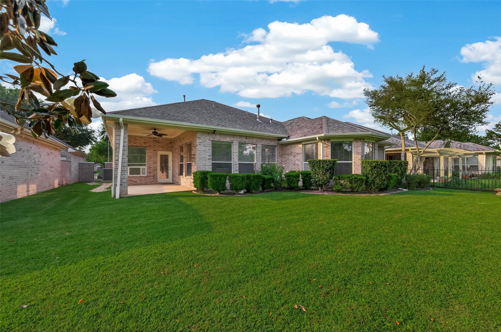 10106 Lost Hollow Lane, Missouri City, TX 77459 This photo showcases a charming brick home with a spacious, well-maintained backyard. It features a covered patio area, perfect for outdoor relaxation, and is surrounded by lush greenery and hedges, creating a serene environment.
