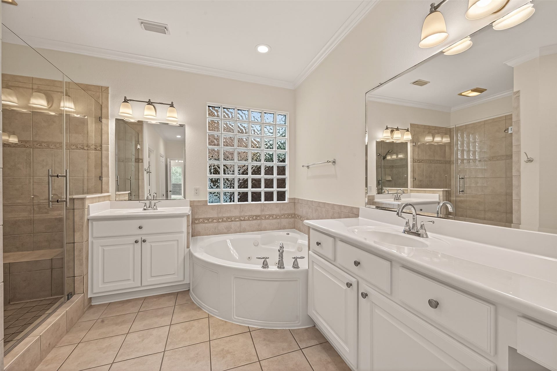 10106 Lost Hollow Lane, Missouri City, TX 77459 This bathroom features a spacious layout with a large bathtub, a glass-enclosed shower, dual sinks with ample counter space, and elegant lighting. The neutral tile work and glass block window add a touch of sophistication.
