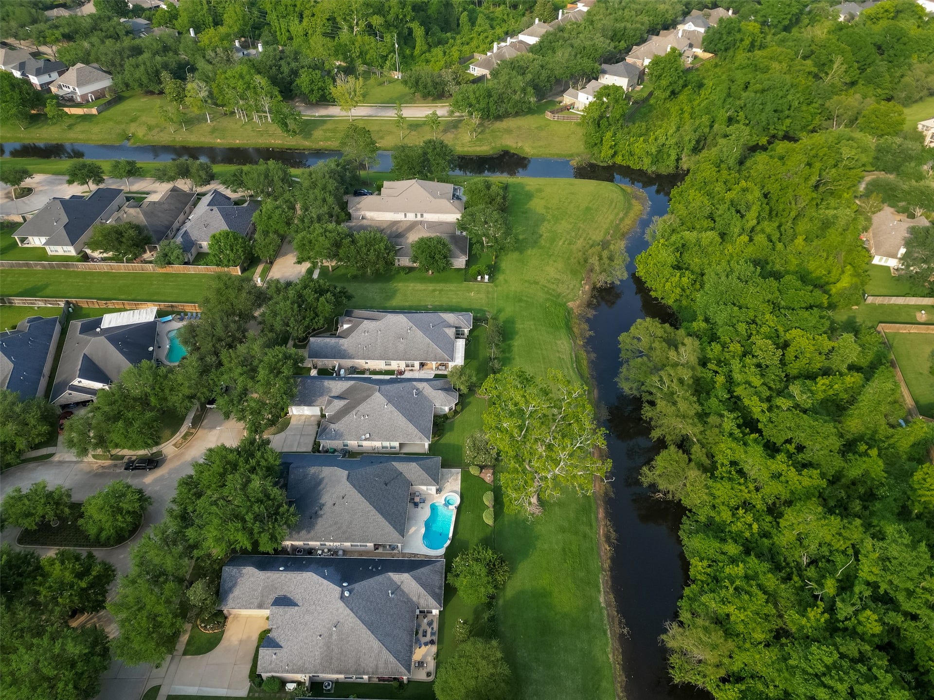 10106 Lost Hollow Lane, Missouri City, TX 77459 This aerial photo showcases a serene neighborhood with well-maintained homes, each with spacious yards. A lush greenbelt and winding creek add natural beauty and privacy, creating an ideal environment for families and nature lovers.