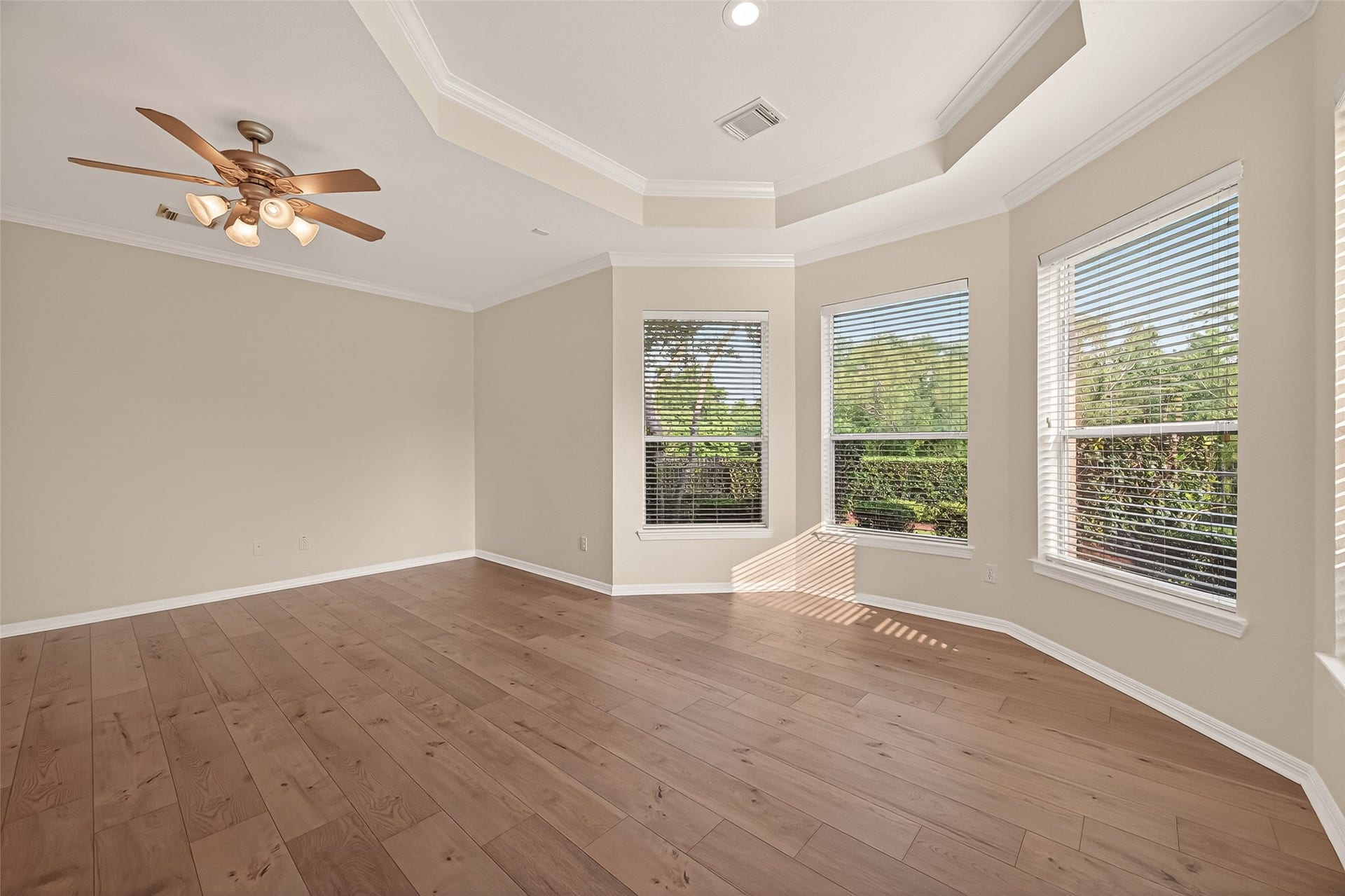 10106 Lost Hollow Lane, Missouri City, TX 77459 This bright, open primary bedroom features hardwood floors, large windows with views of greenery, a ceiling fan, and a tray ceiling for added elegance.