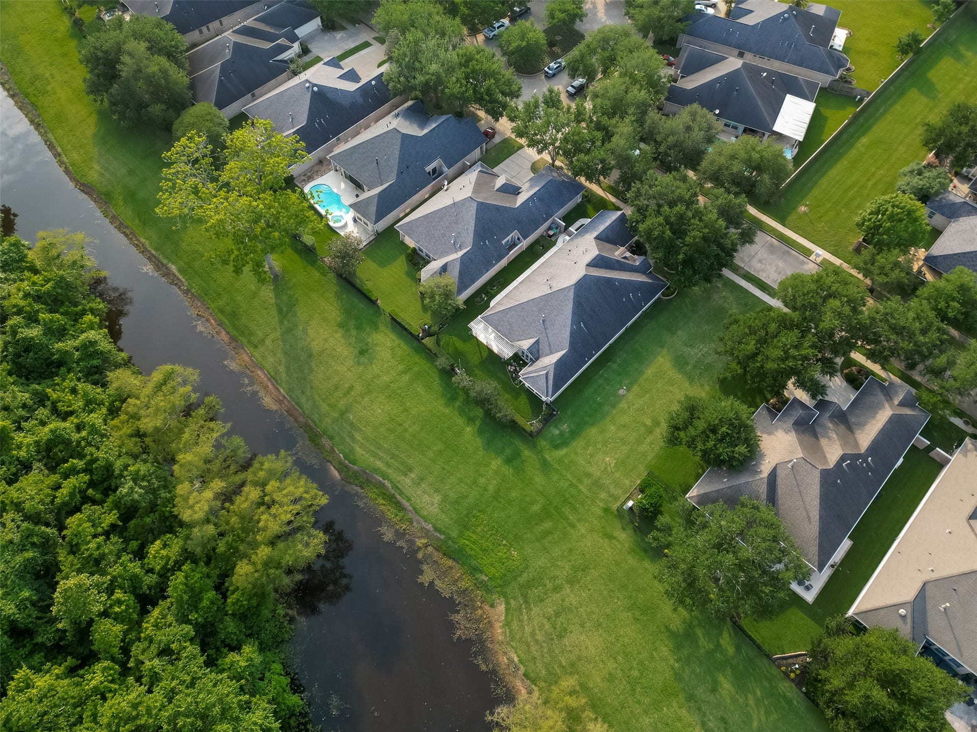 10106 Lost Hollow Lane, Missouri City, TX 77459 This aerial view showcases a serene neighborhood with well-maintained homes, spacious backyards, and lush greenery. the area is bordered by a tree-lined waterway, offering a peaceful, natural setting.