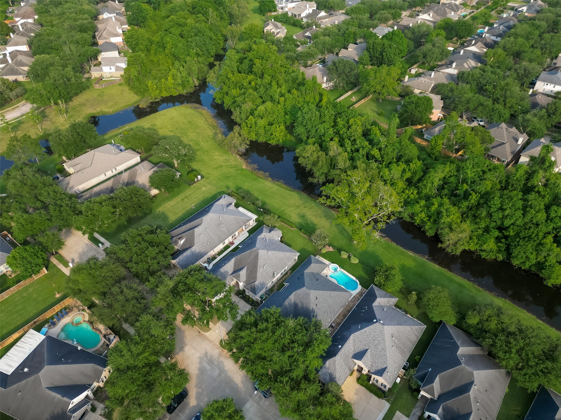 10106 Lost Hollow Lane, Missouri City, TX 77459 This aerial photo showcases a suburban neighborhood with well-maintained homes. The area is lush with greenery and bordered by a small waterway, offering a serene and picturesque environment.