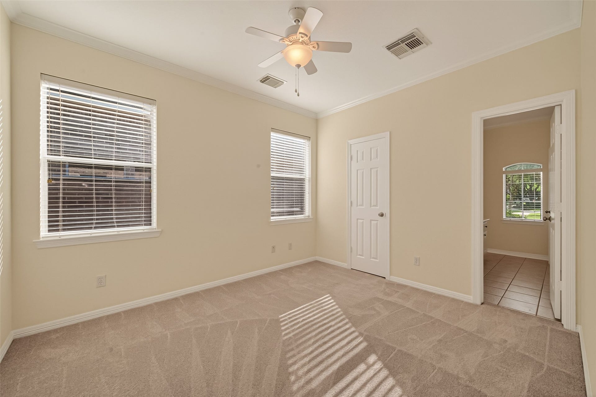 10106 Lost Hollow Lane, Missouri City, TX 77459 This room features soft beige walls, two windows with blinds allowing natural light, plush carpeting, and a ceiling fan. It includes a closet and an adjoining tiled bathroom, creating a cozy and functional space.