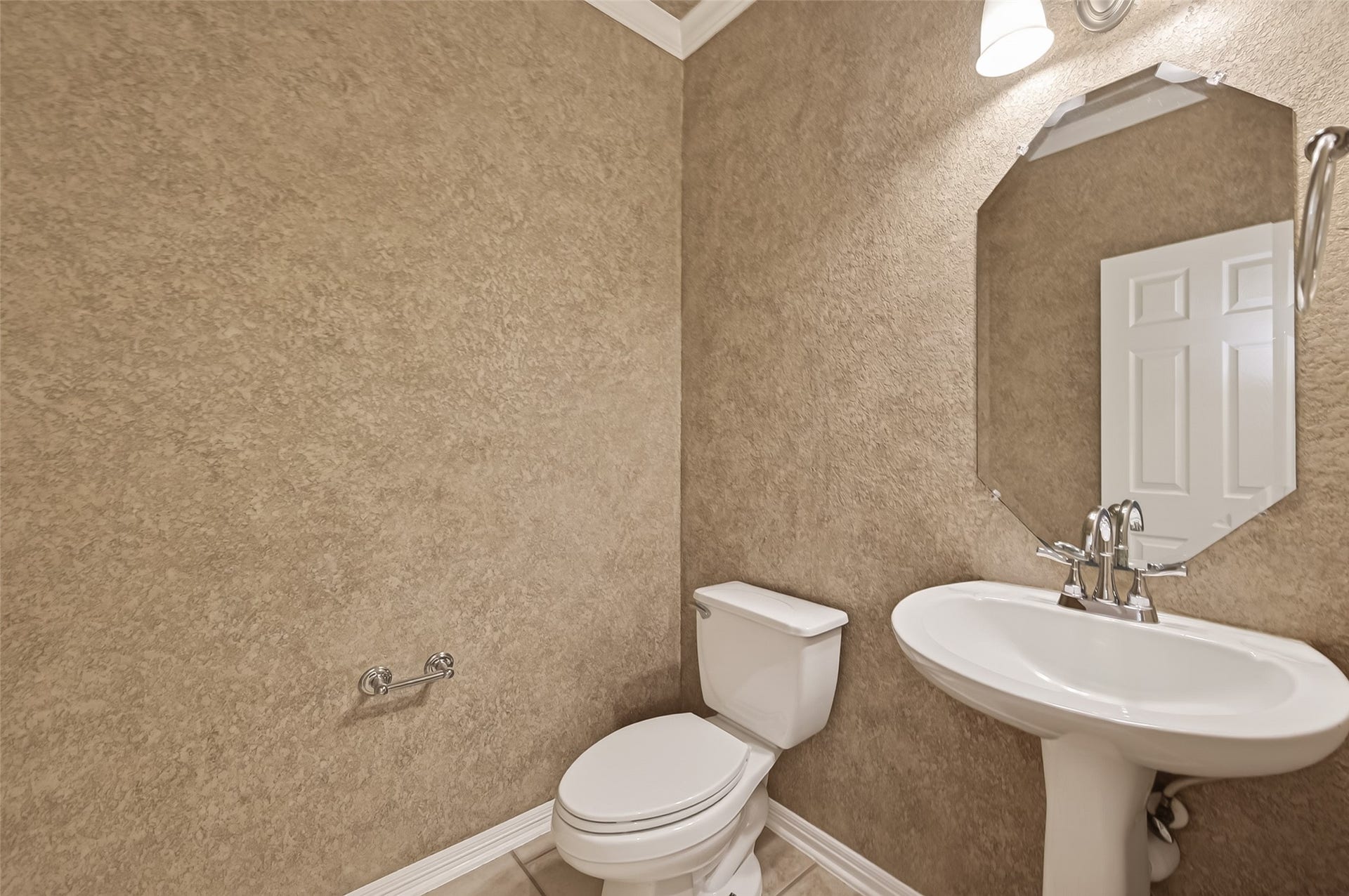 10106 Lost Hollow Lane, Missouri City, TX 77459 Half, well-lit bathroom featuring a pedestal sink, toilet, octagonal mirror, and textured beige walls, ideal for guest use.