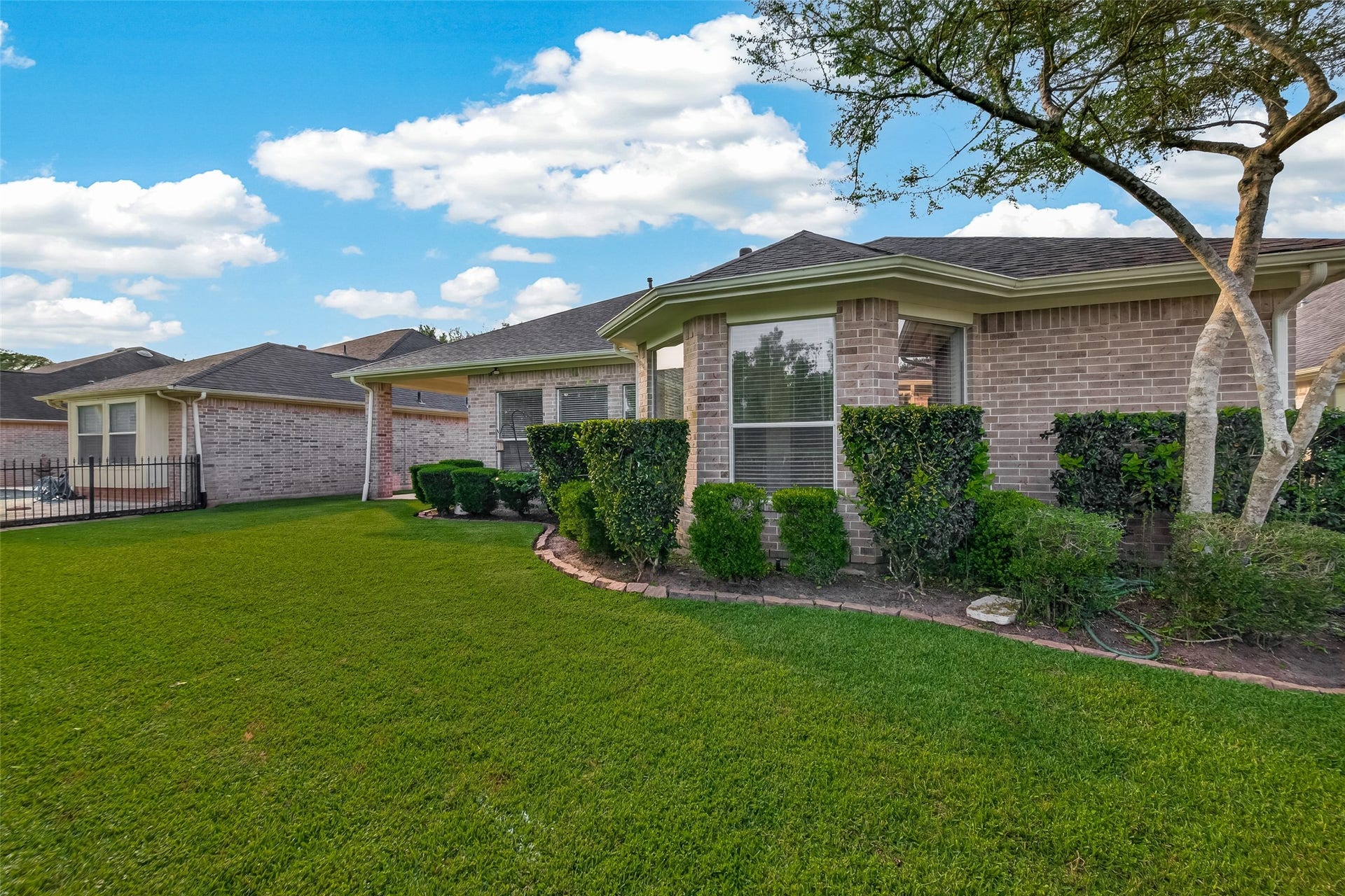 10106 Lost Hollow Lane, Missouri City, TX 77459 This photo showcases a well-maintained brick home with manicured hedges and a lush green lawn. The house features large windows and a modern roof, offering a welcoming and attractive exterior.
