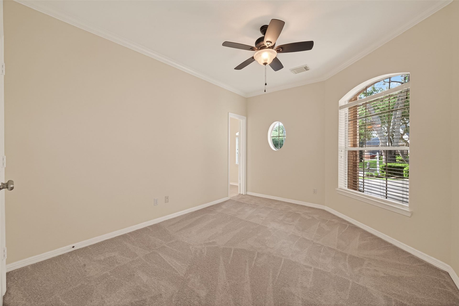 10106 Lost Hollow Lane, Missouri City, TX 77459 Bright and spacious bedroom with neutral-colored walls and new carpet, featuring an arched window for natural light and a ceiling fan for comfort.