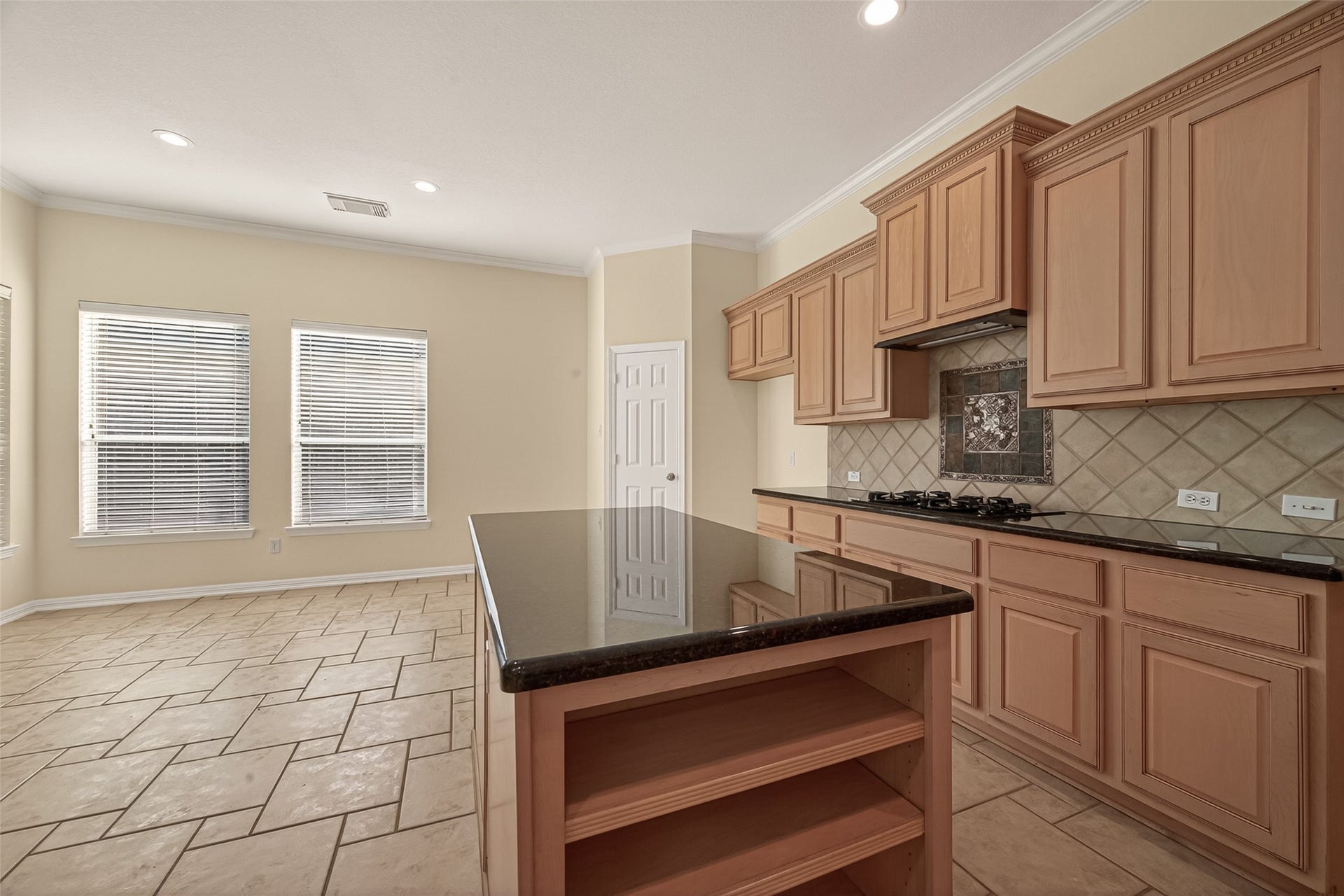 10106 Lost Hollow Lane, Missouri City, TX 77459 Bright kitchen with tile flooring, ample natural light, and wooden cabinets. Features a large island with dark countertops and modern appliances, creating an inviting space for cooking and dining.