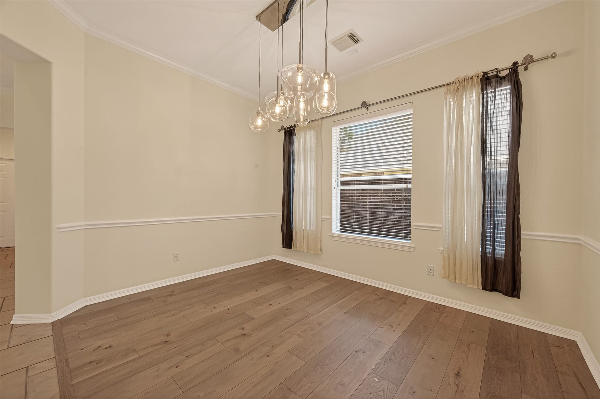 10106 Lost Hollow Lane, Missouri City, TX 77459 Bright dining room with hardwood floors, neutral walls, and a contemporary light fixture. Features a large window with sheer and dark curtains, offering natural light.