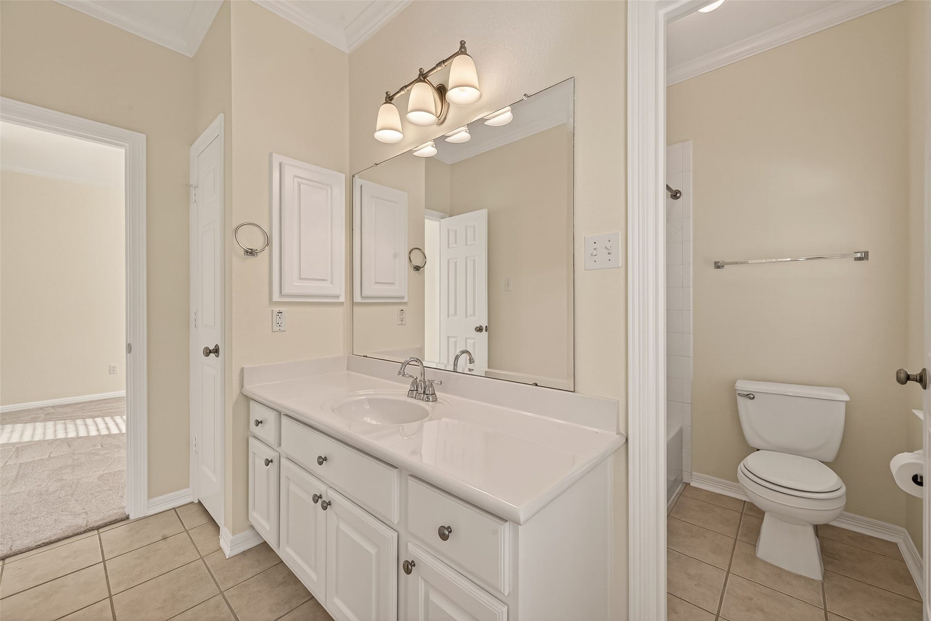 10106 Lost Hollow Lane, Missouri City, TX 77459 This is a bright, clean bathroom featuring a large mirror above a white vanity with ample storage, modern light fixtures, and a toilet. The room has neutral tile flooring and walls, offering a fresh and inviting space.