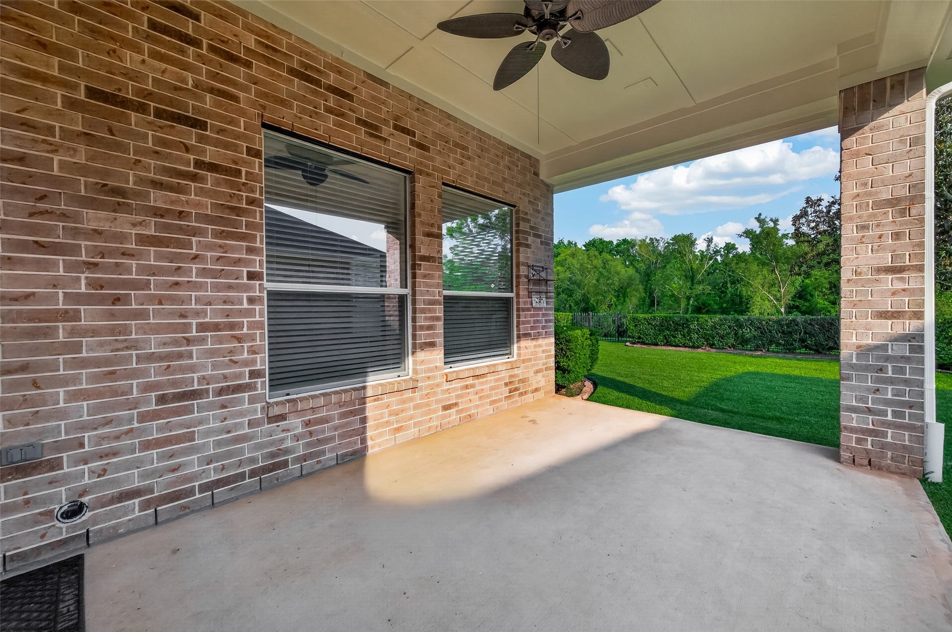 10106 Lost Hollow Lane, Missouri City, TX 77459 This photo showcases a covered patio with brick walls and a ceiling fan, overlooking a lush green backyard. Ideal for outdoor relaxation and entertaining.