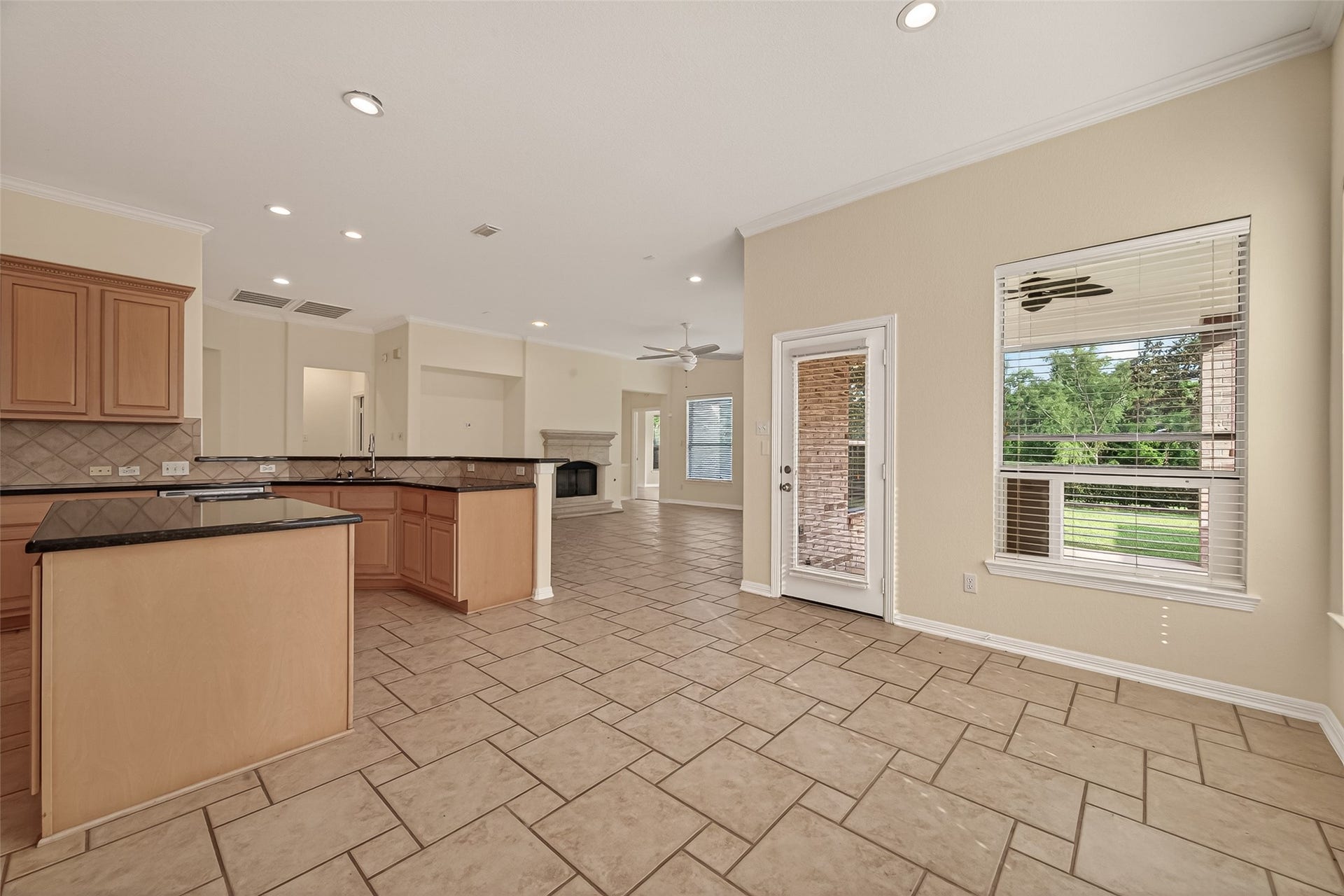 10106 Lost Hollow Lane, Missouri City, TX 77459 This spacious, open-concept kitchen and living area features tiled flooring, a central island with granite countertops, and warm wood cabinetry. A cozy fireplace is visible in the living space, and large windows provide ample natural light. The area leads to an outdoor view through a glass door, enhancing the bright, welcoming atmosphere.